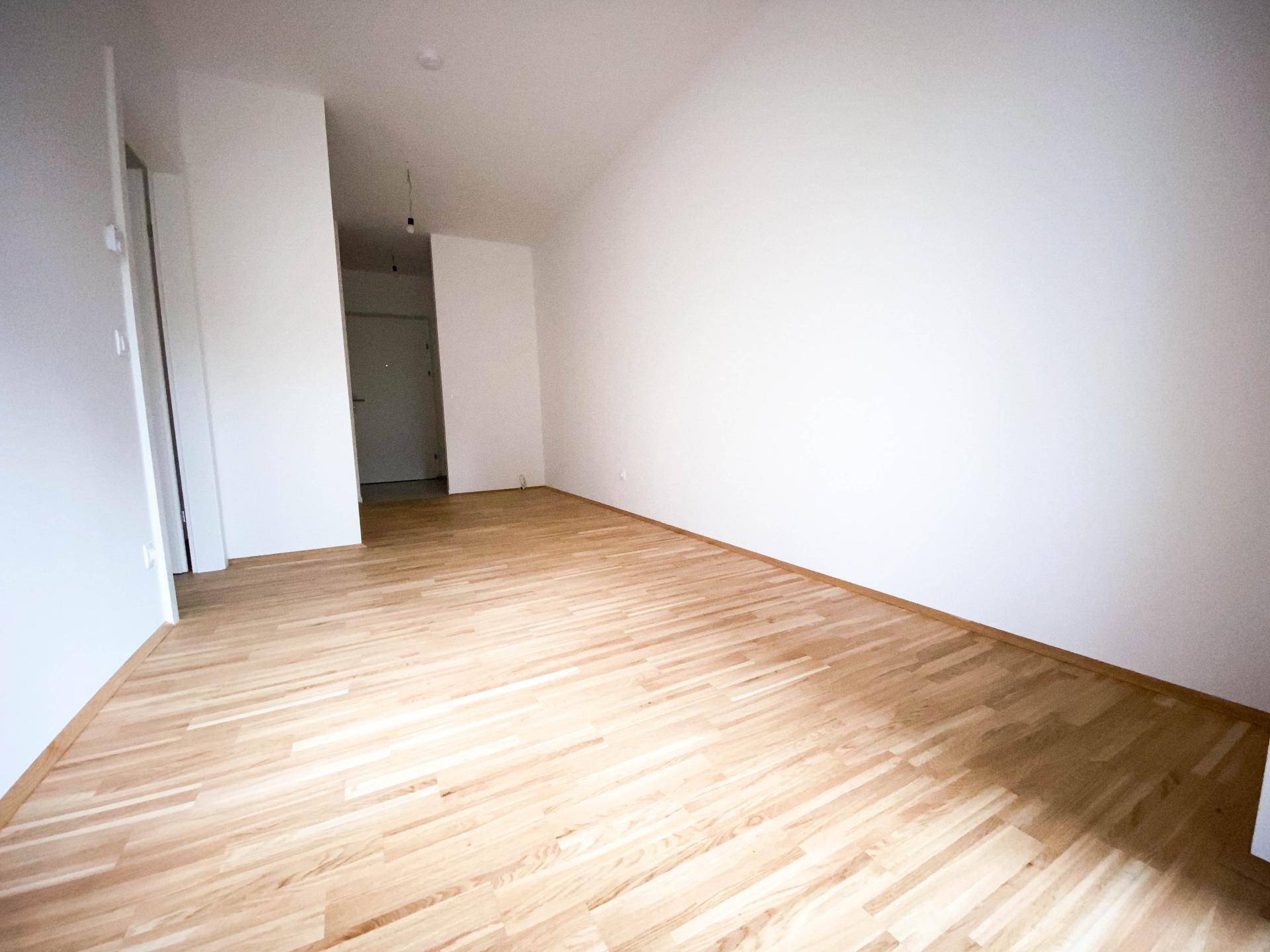 Leerer Wohnbereich mit hellem Parkettboden und weißen Wänden, bereit zur individuellen Gestaltung.