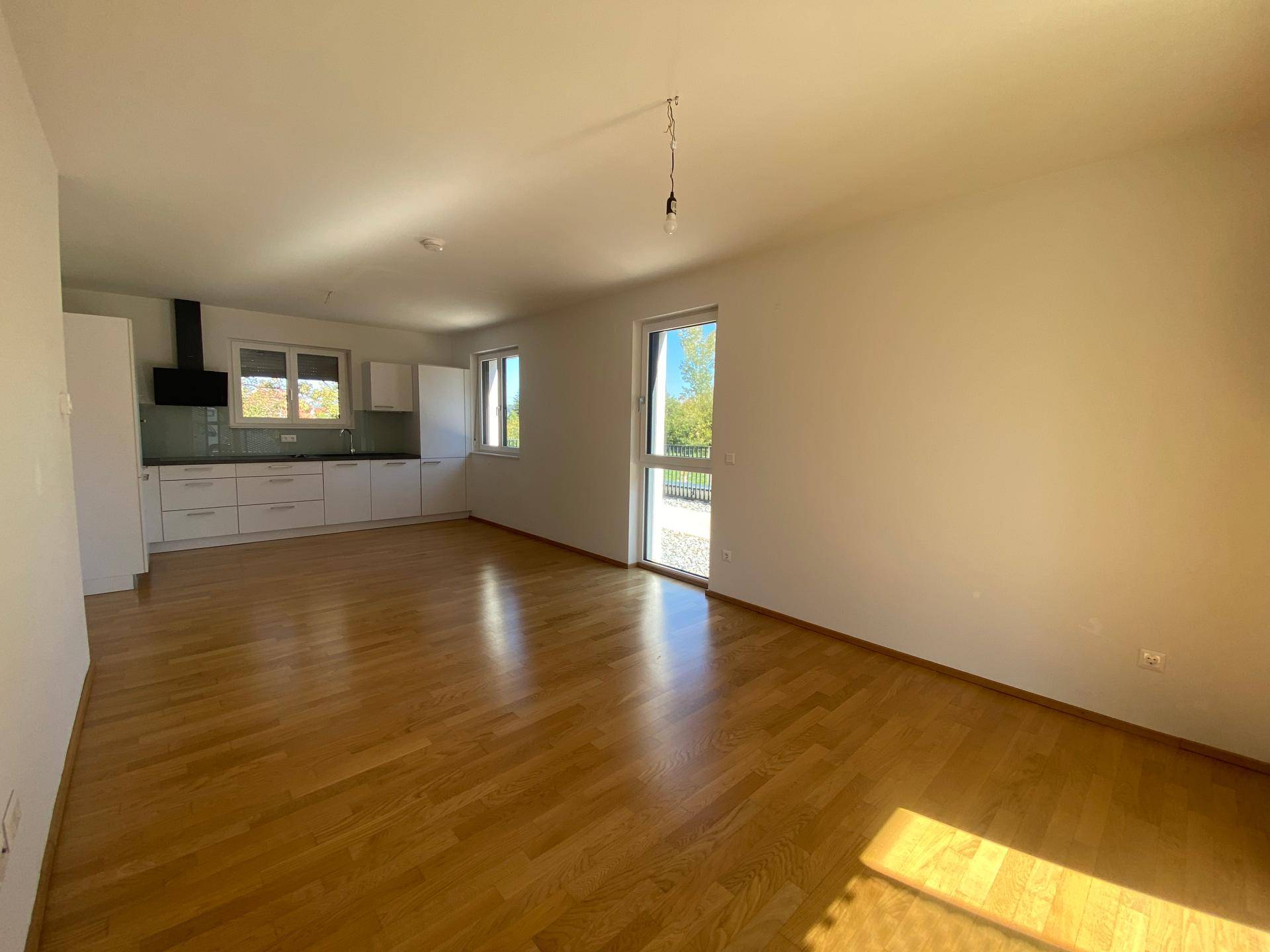 Geräumiger Wohn- und Essbereich mit Holzboden, offener Küche und Zugang zum Außenbereich.