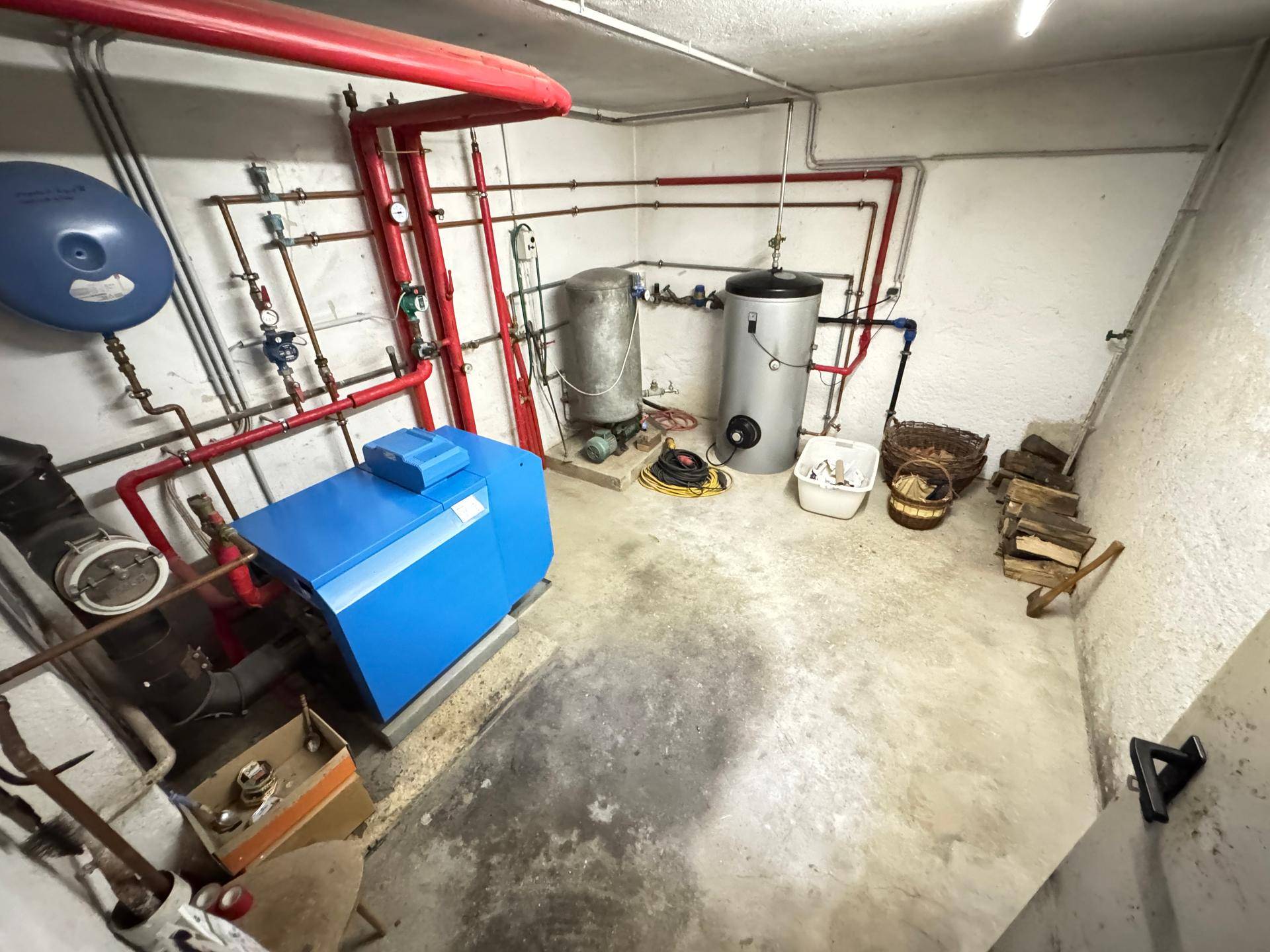 Heizungsraum im Keller mit blauer Heizungsanlage, Warmwasserspeichern und sichtbaren Rohren.