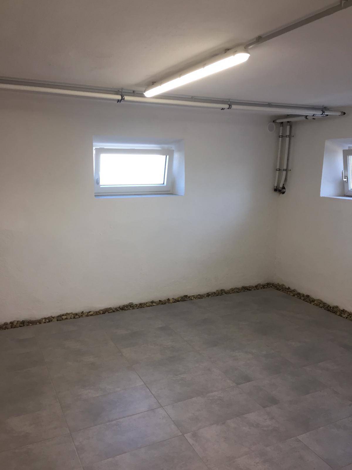 Heller Kellerraum mit Fliesenboden und kleinem Fenster, ideal für Lagerzwecke.