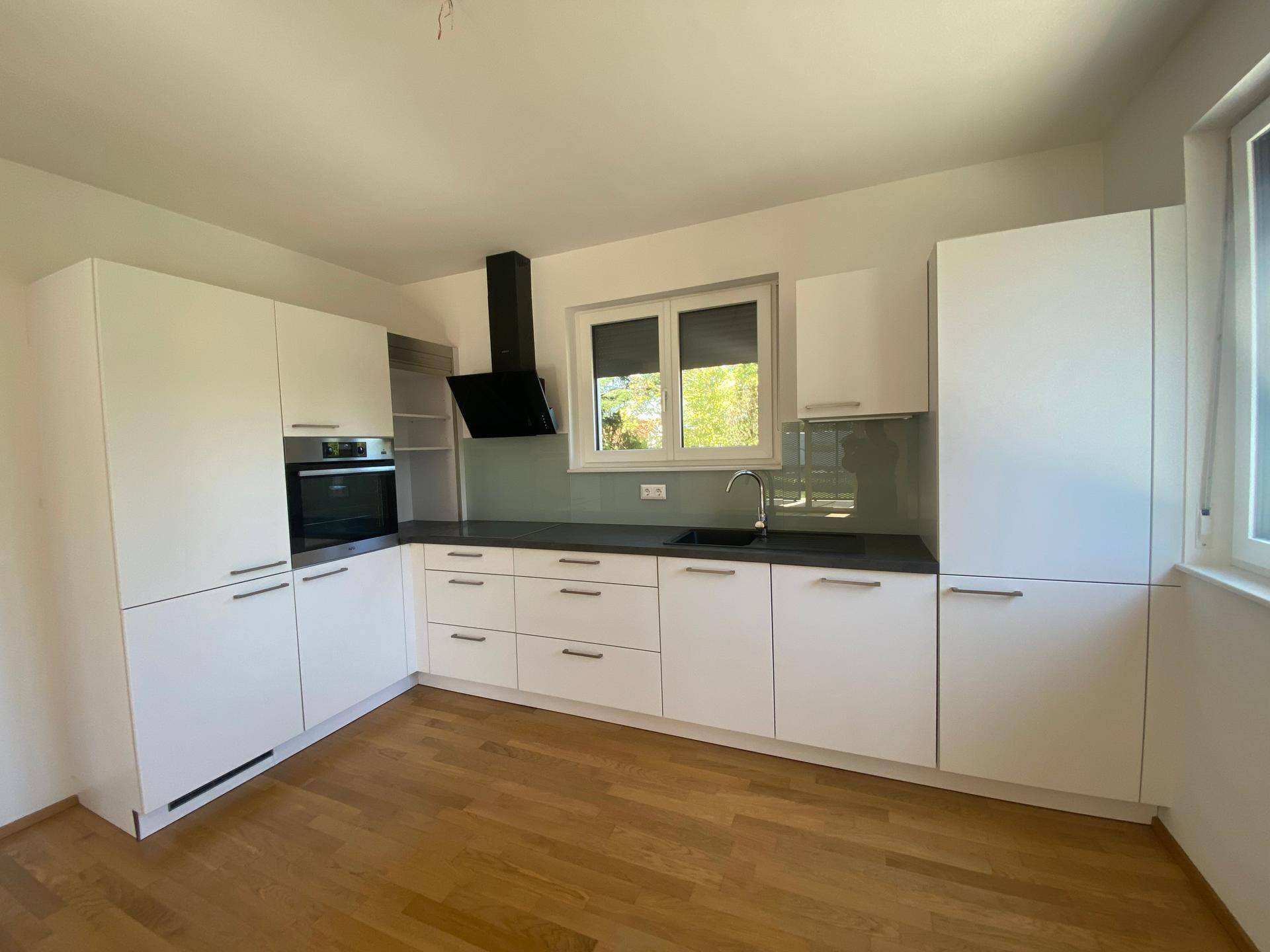 Helle Einbauküche mit weißen Fronten, integriertem Backofen und großem Fenster für viel Tageslicht.