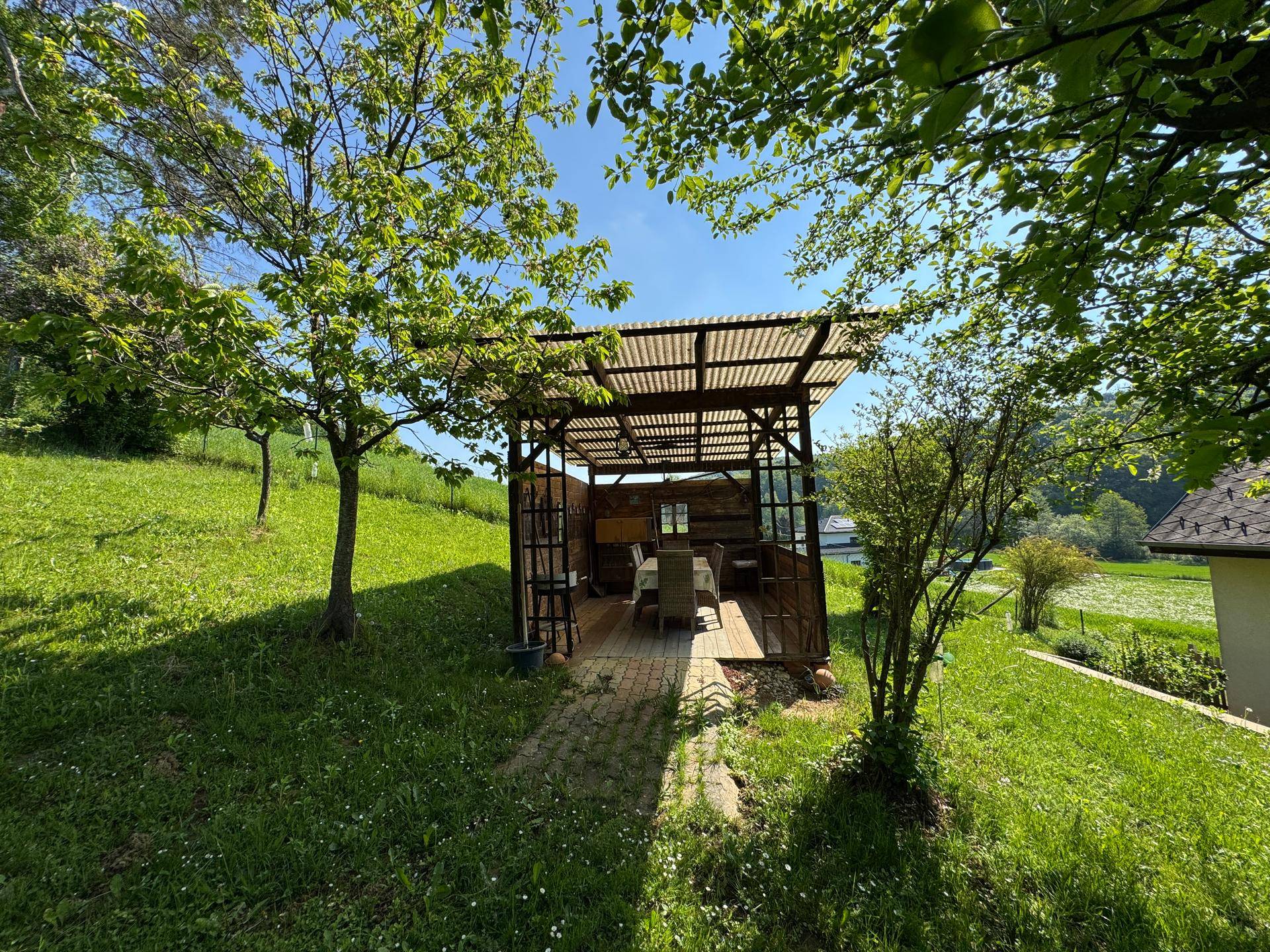 Gemütlicher Sitzbereich im Garten unter einer Pergola, umgeben von viel Grün.