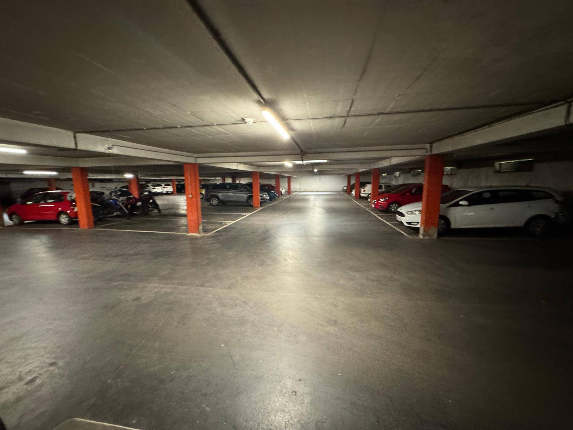 Geräumige Tiefgarage mit zahlreichen Stellplätzen für Autos und Motorräder unter künstlicher Beleuchtung.