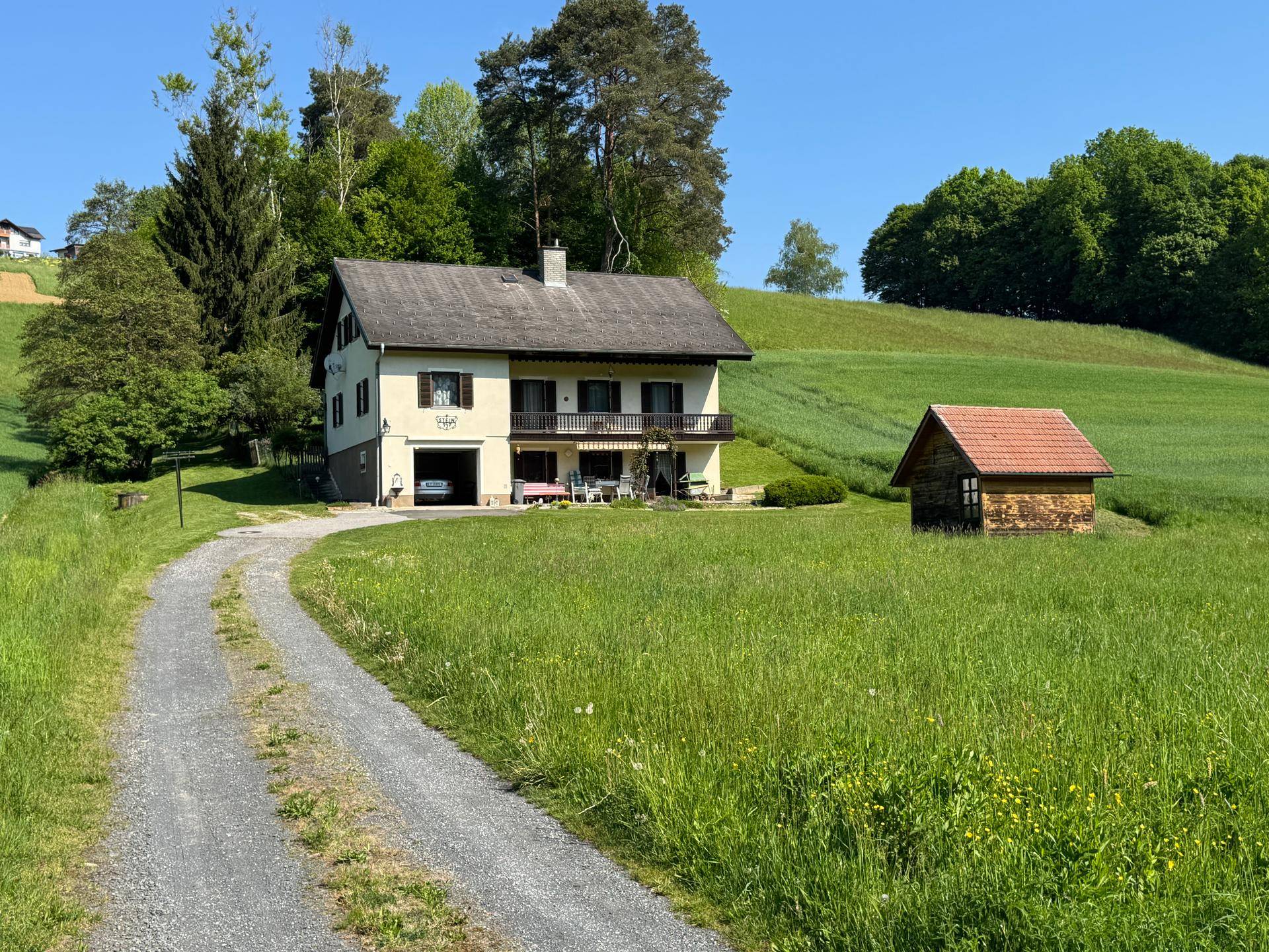 Landhaus mit Zufahrt und Gartenhaus, eingebettet in eine idyllische grüne Landschaft.