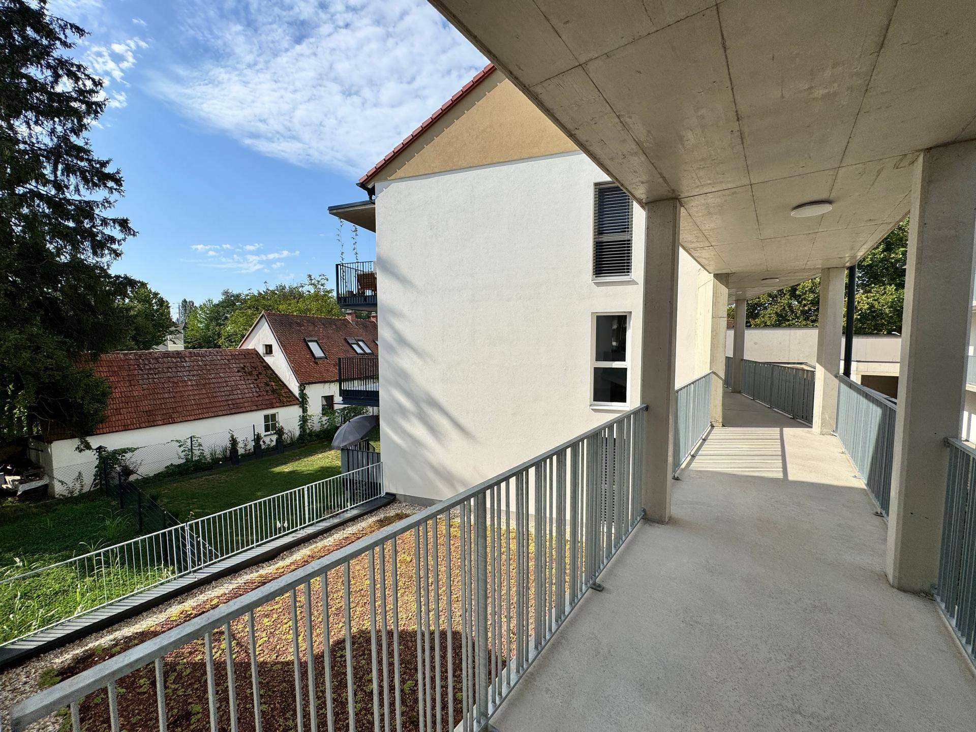 Überdachter Außenflur mit Geländer und Blick auf die umliegende Wohnbebauung.