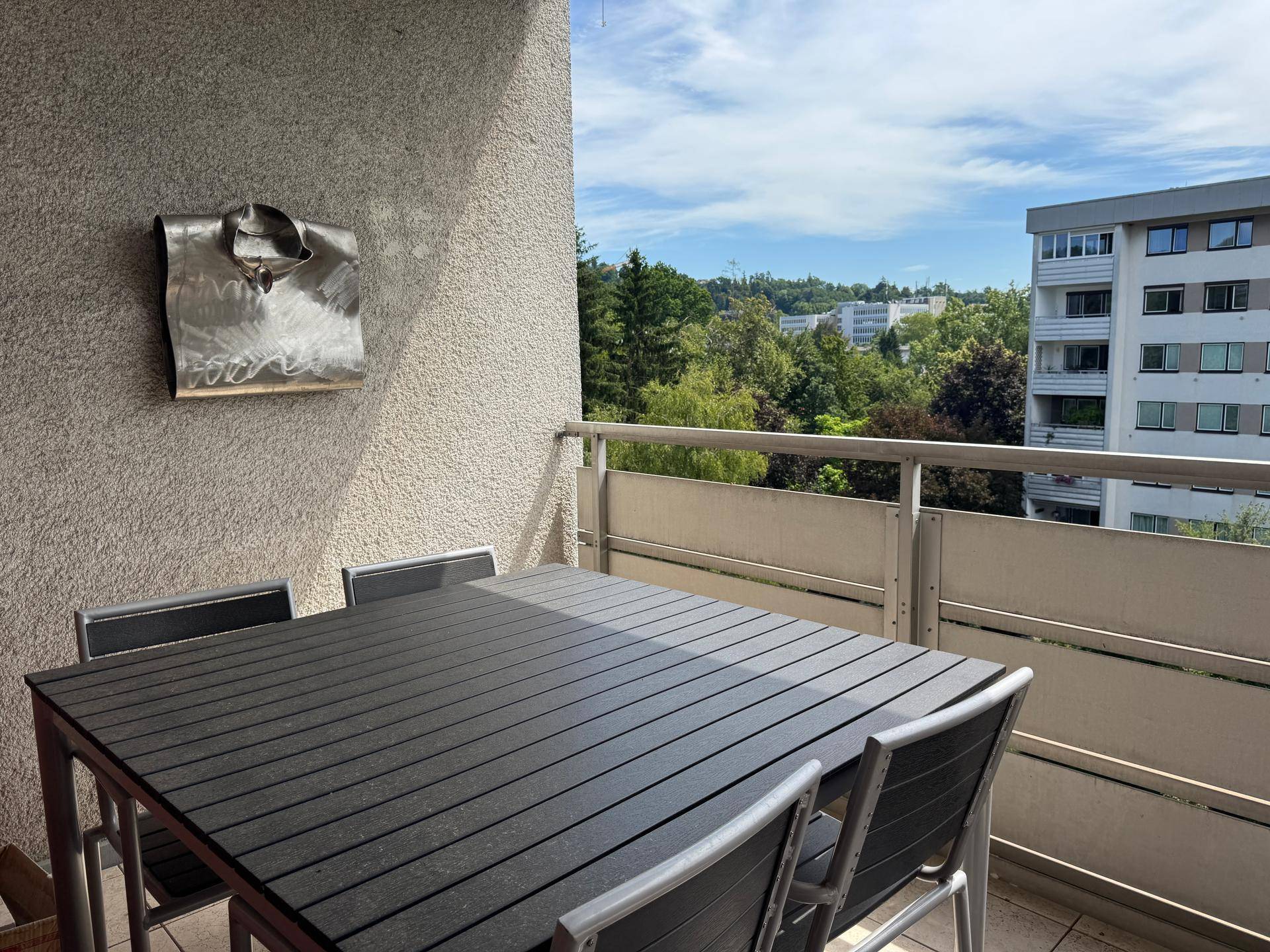 Möblierter Balkon mit Esstisch und Stühlen, bietet einen Blick ins Grüne.