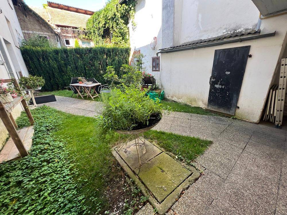 Begrünter Innenhof mit Hecke, Sitzbereich und Zugang zu einem Nebengebäude.