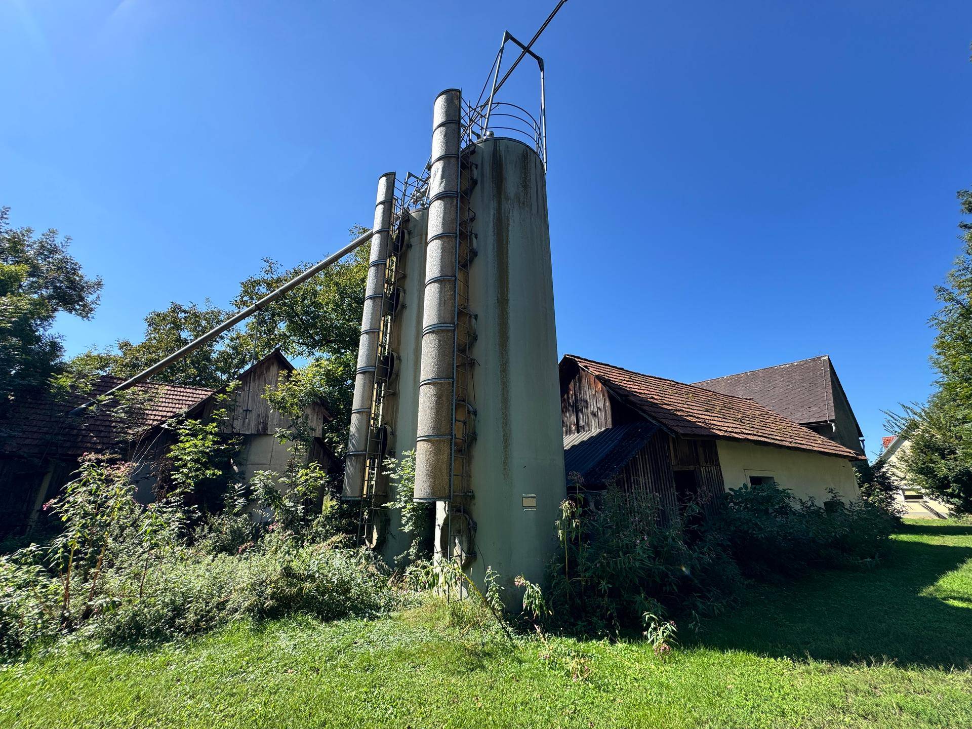 Alte Silos und Nebengebäude auf einem ländlichen Grundstück unter blauem Himmel.