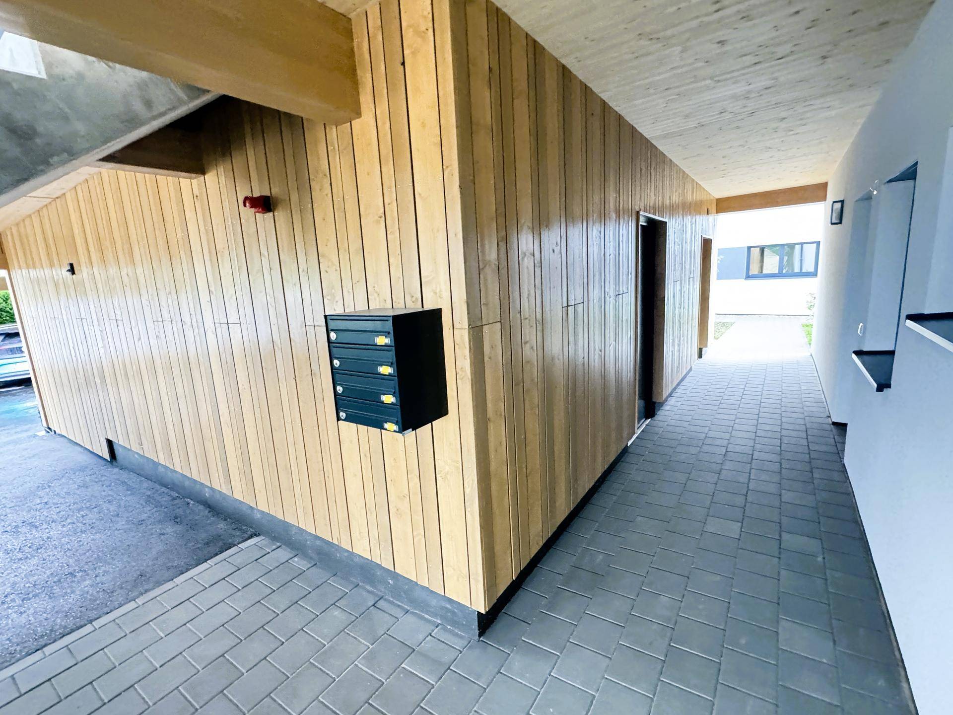 Überdachter Eingangsbereich mit Holzverkleidung und Briefkästen in einem modernen Gebäude.
