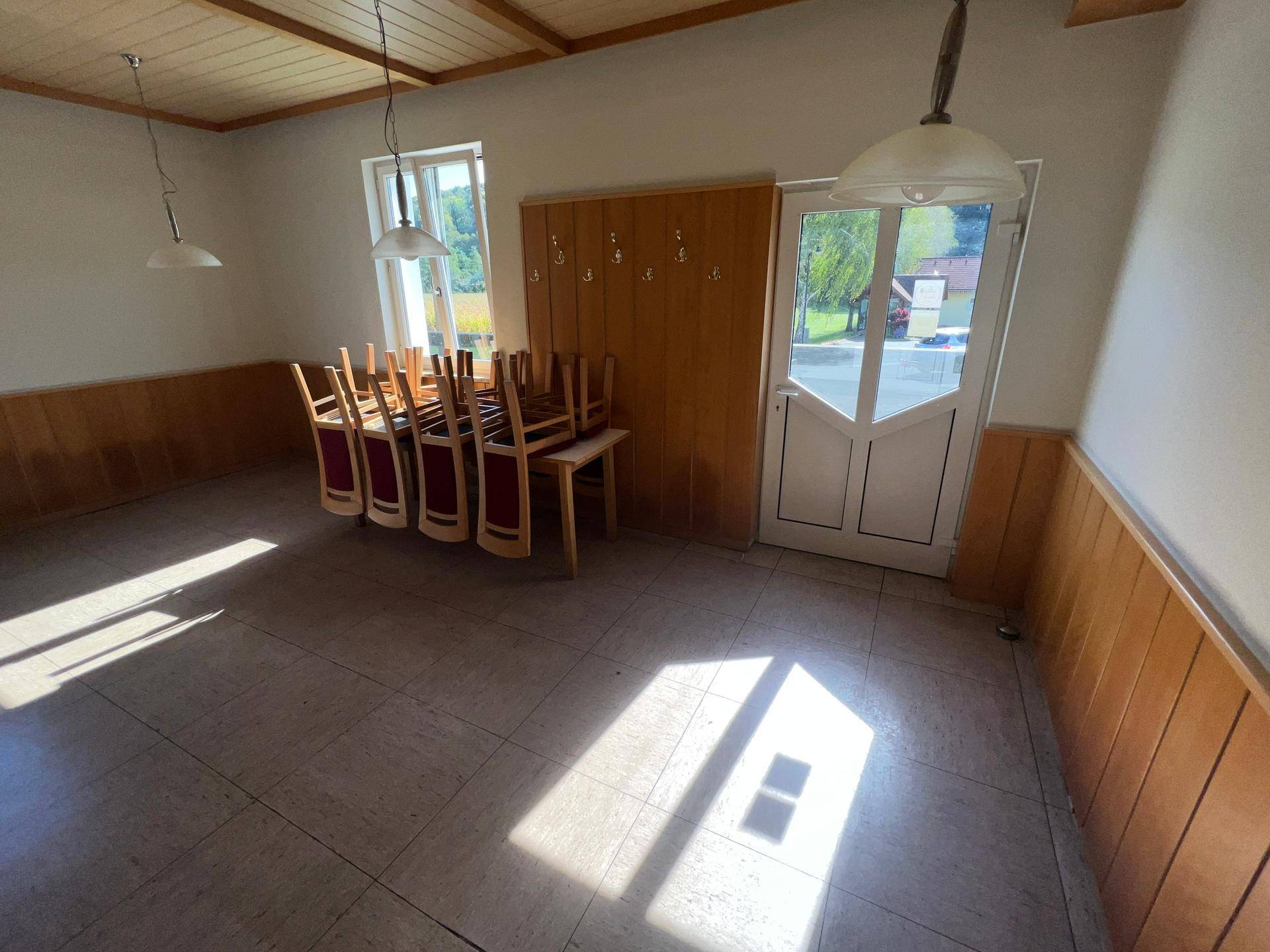 Geräumiger Speisesaal mit Holztäfelung, Fliesenboden und viel Tageslicht durch große Fenster.