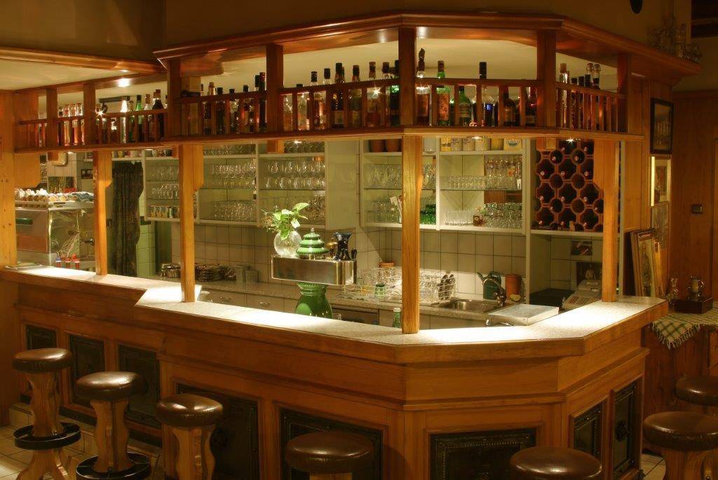 Traditionelle Bar mit Holztheke, Barhockern und Regalen voller Flaschen und Gläser.