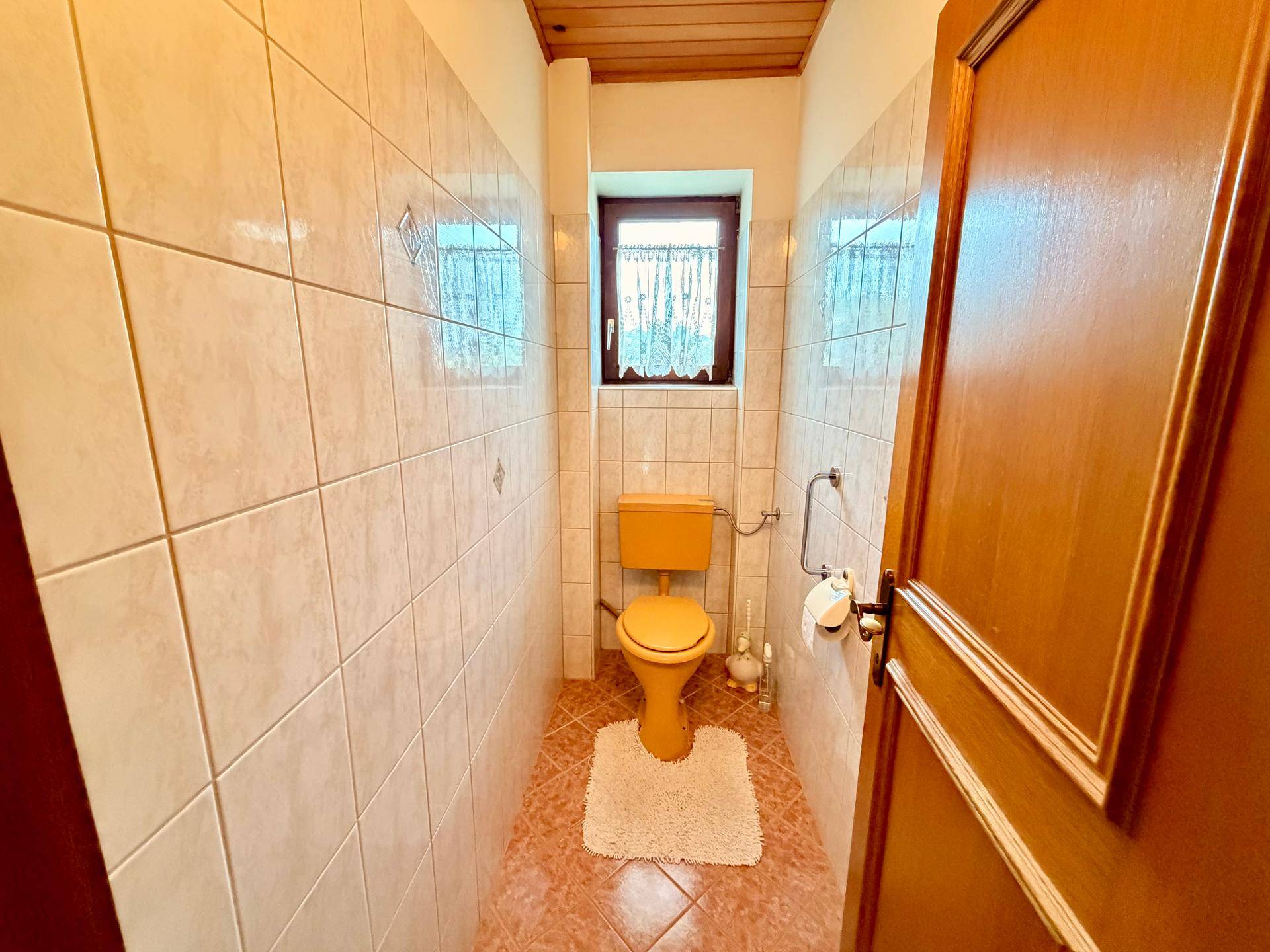 Separate Toilette mit gelbem WC, kleinen Fliesen und Fenster, funktional und hell.