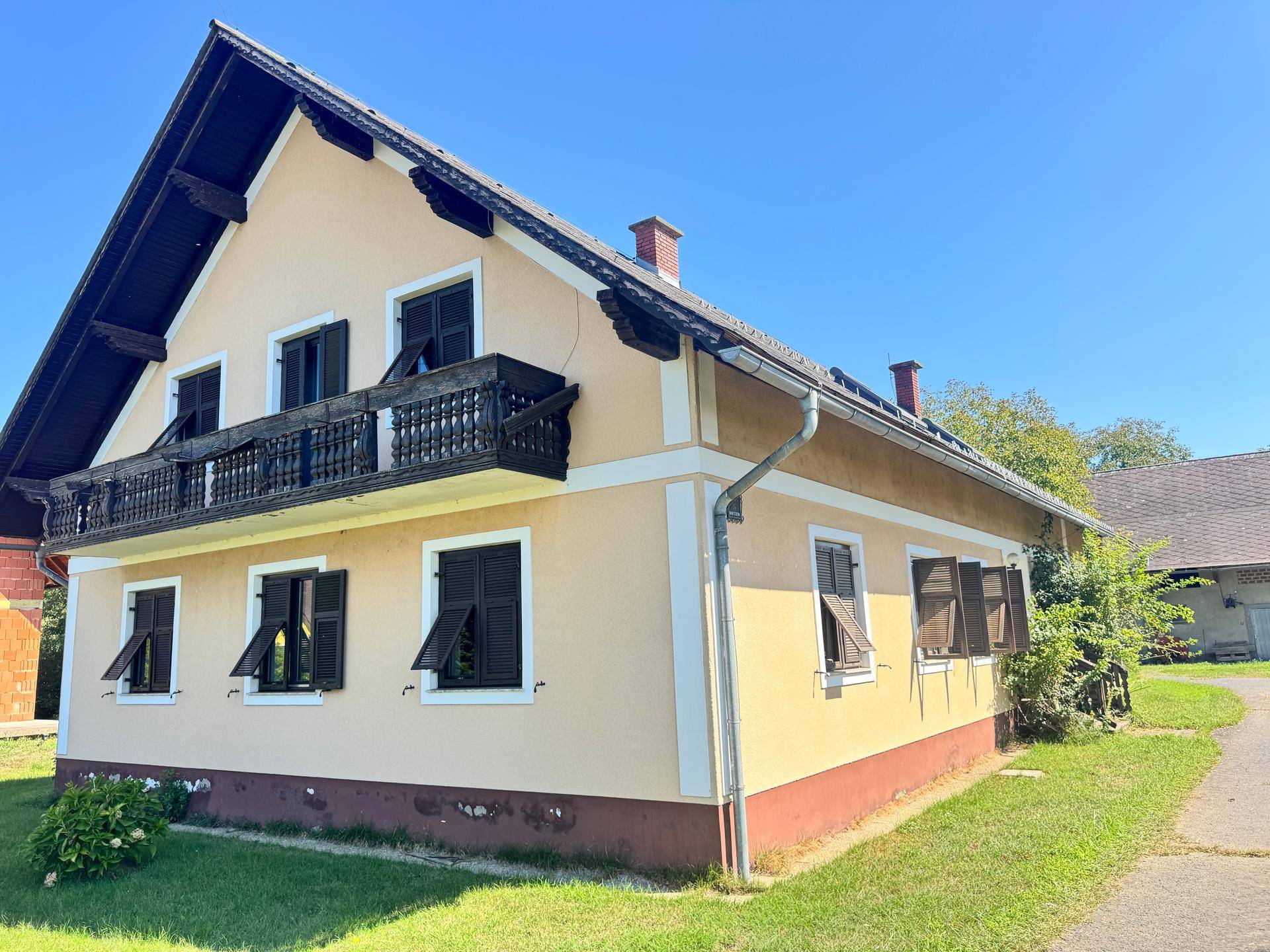 Seitenansicht des Hauses mit Balkon, Fensterläden und Regenrinne an einem sonnigen Tag.
