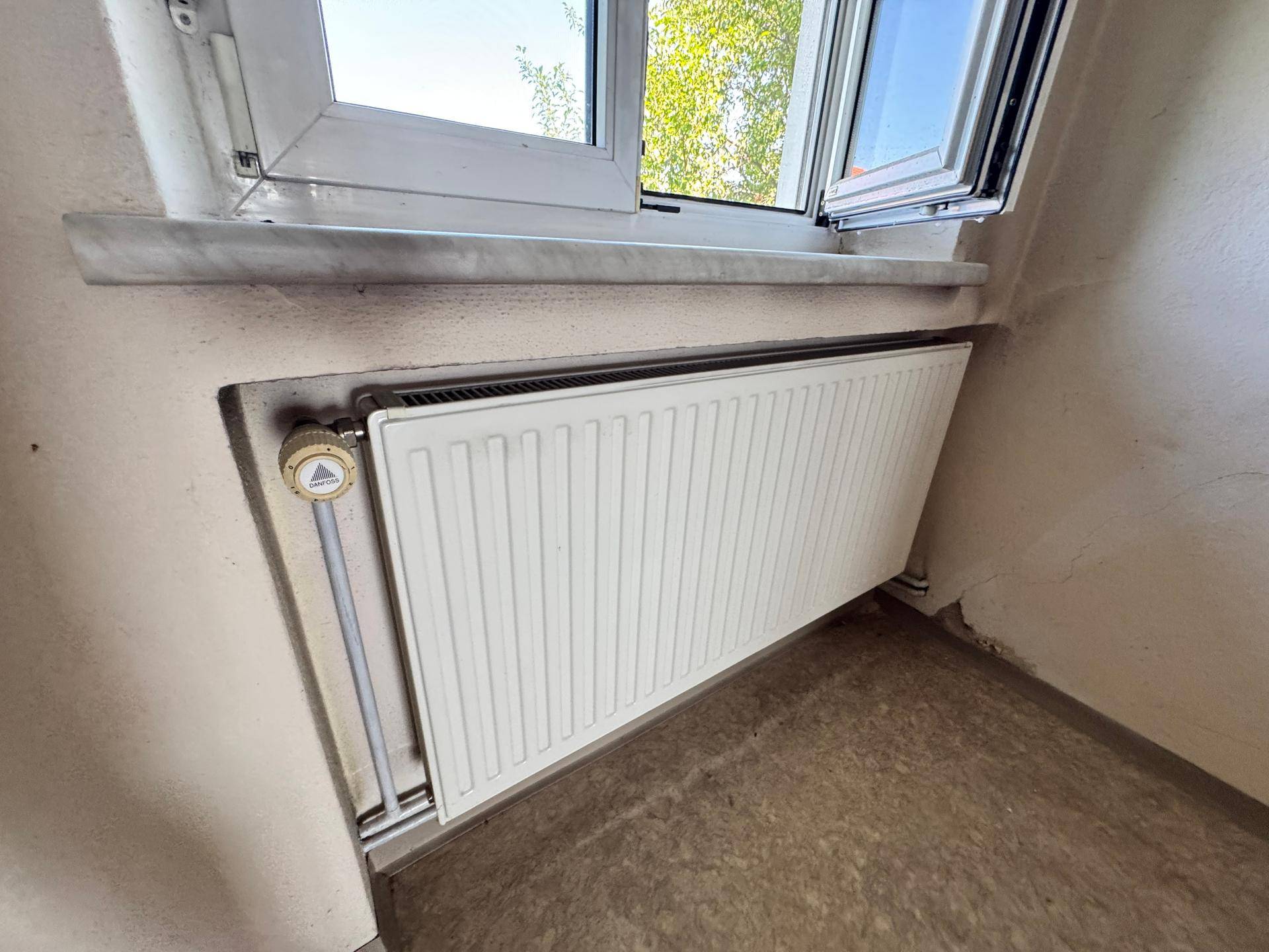 Nahaufnahme eines Heizkörpers unter einem Fenster mit hellem Bodenbelag.