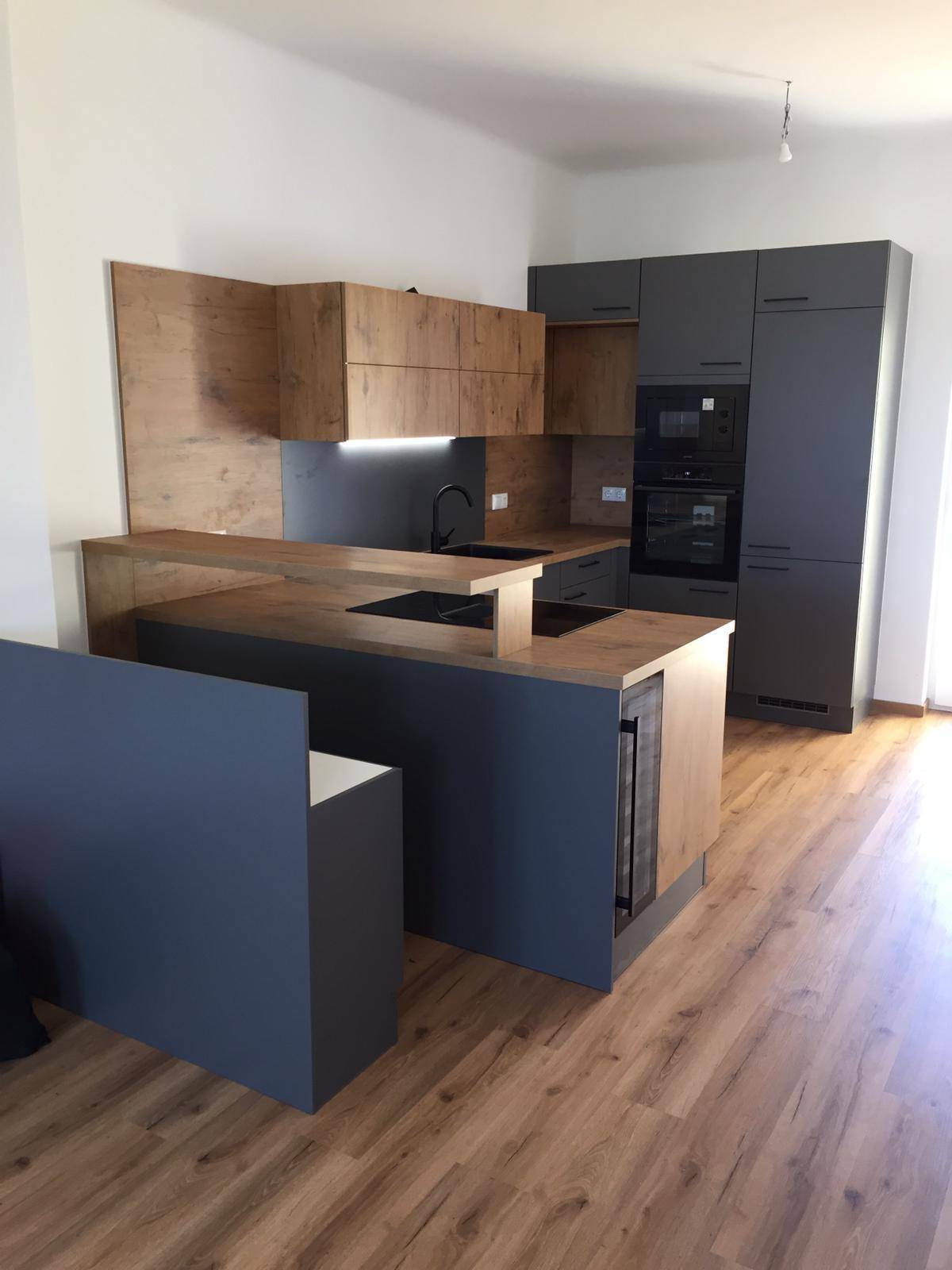 Offene, moderne Küche mit Holzoptik-Elementen, grauen Fronten und integrierten Geräten.