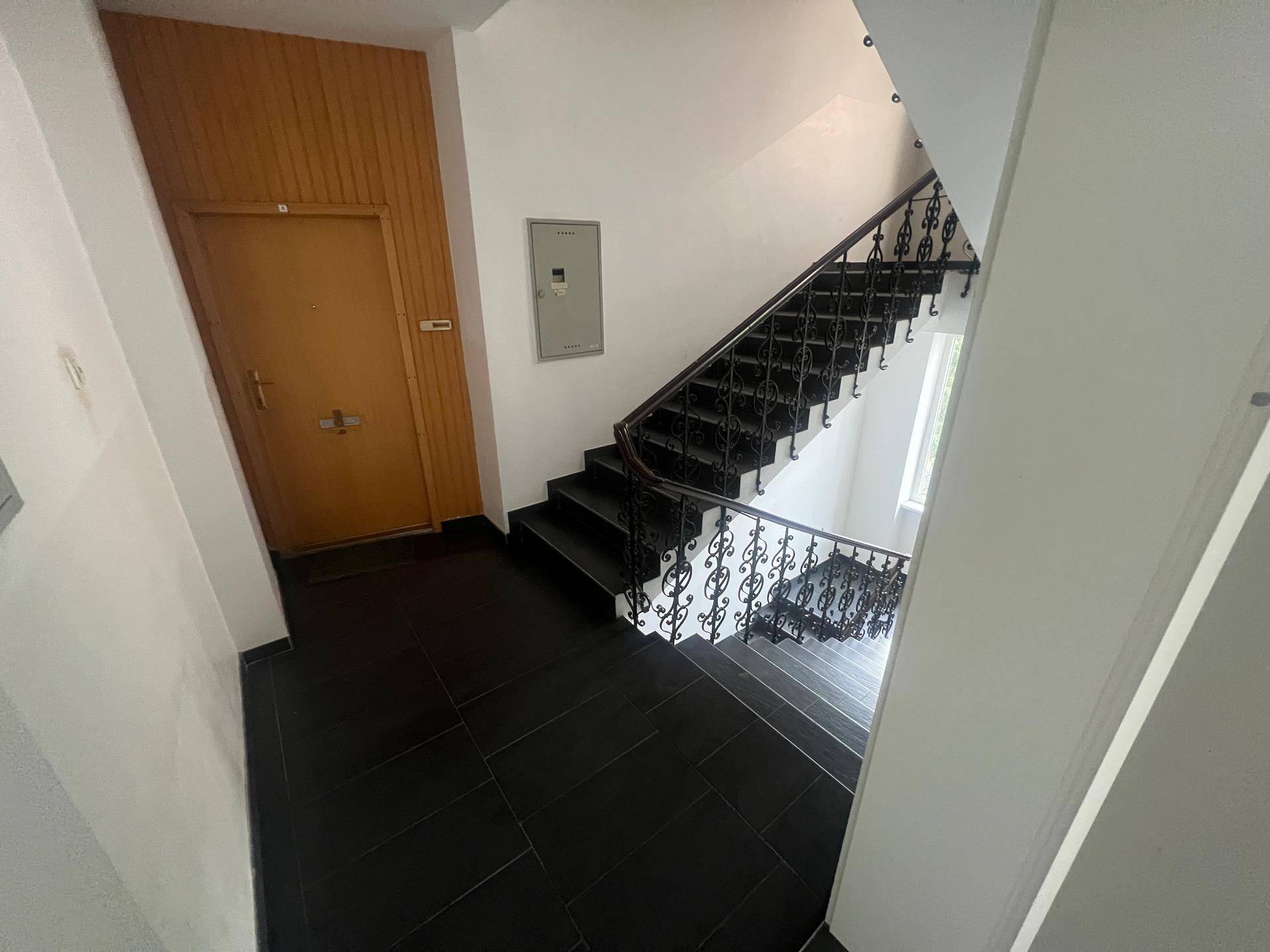 Treppenhaus mit dunklen Fliesen und einem schmiedeeisernen Geländer in einem Altbau.