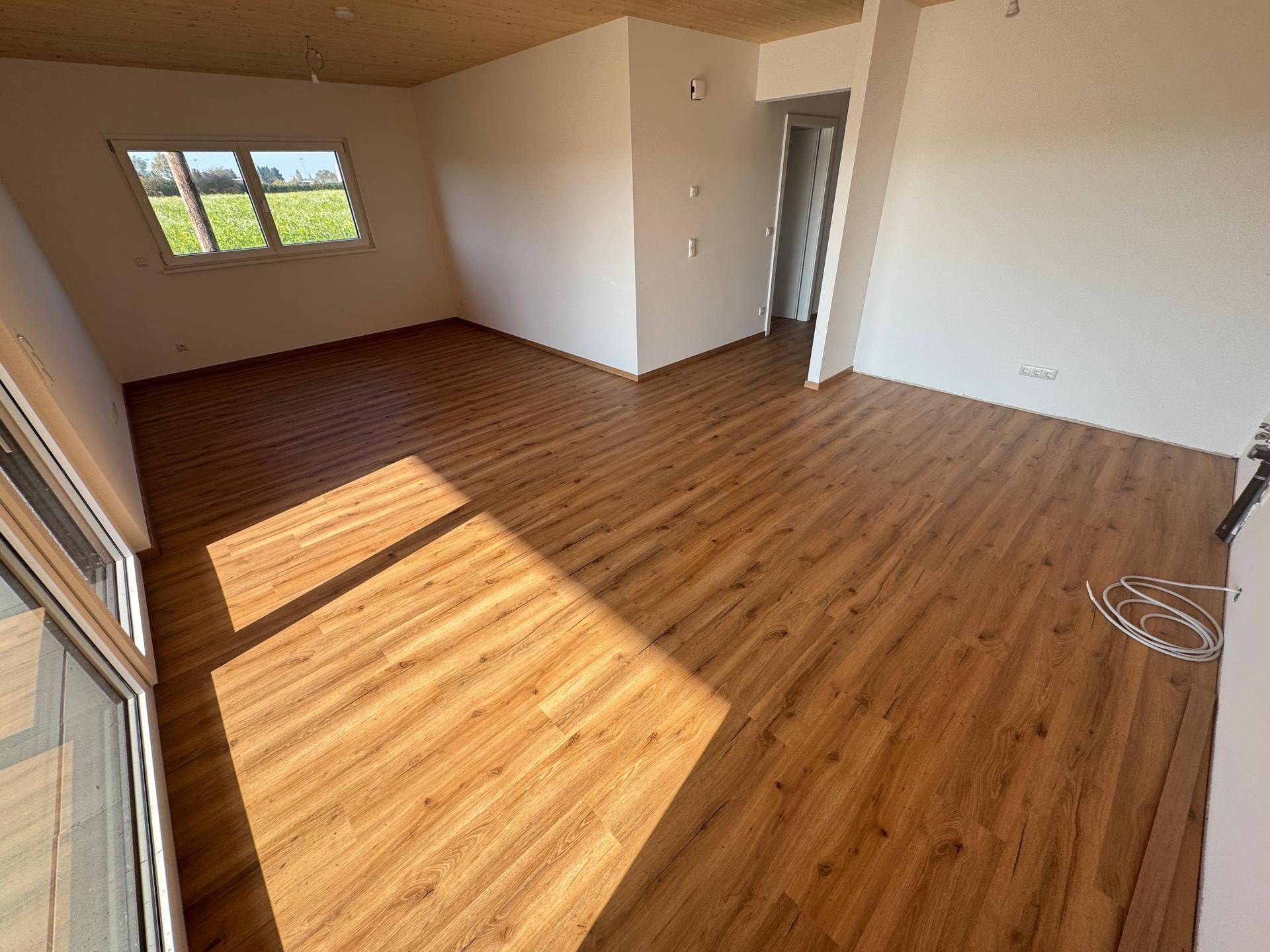 Heller Wohnbereich mit Laminatboden und Zugang zu einem Balkon, ideal für Entspannung.