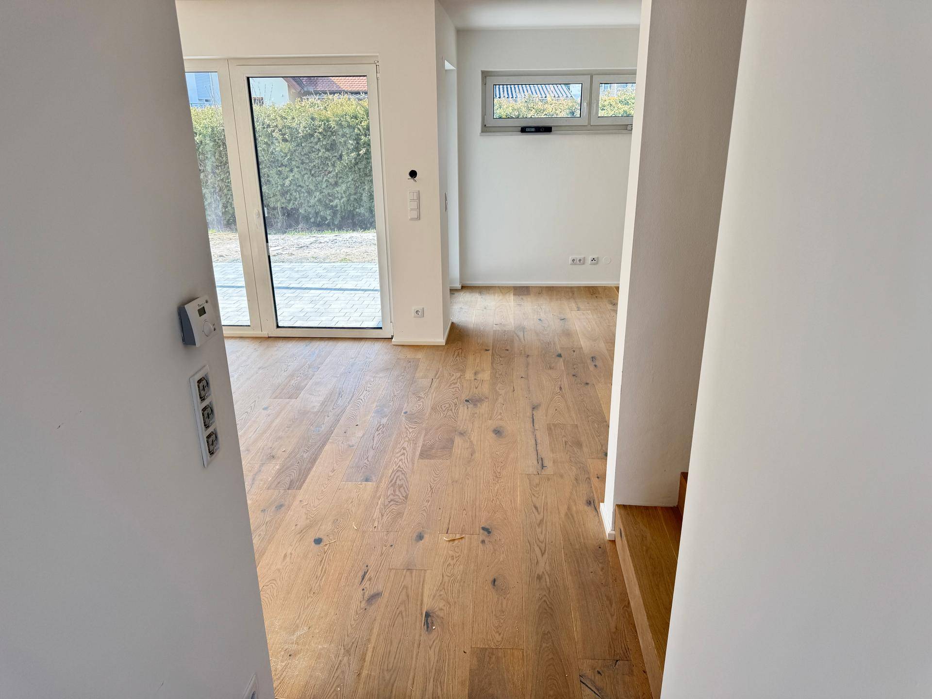 Heller Raum mit Holzboden und großen Fenstern, die den Zugang zum Gartenbereich bieten.