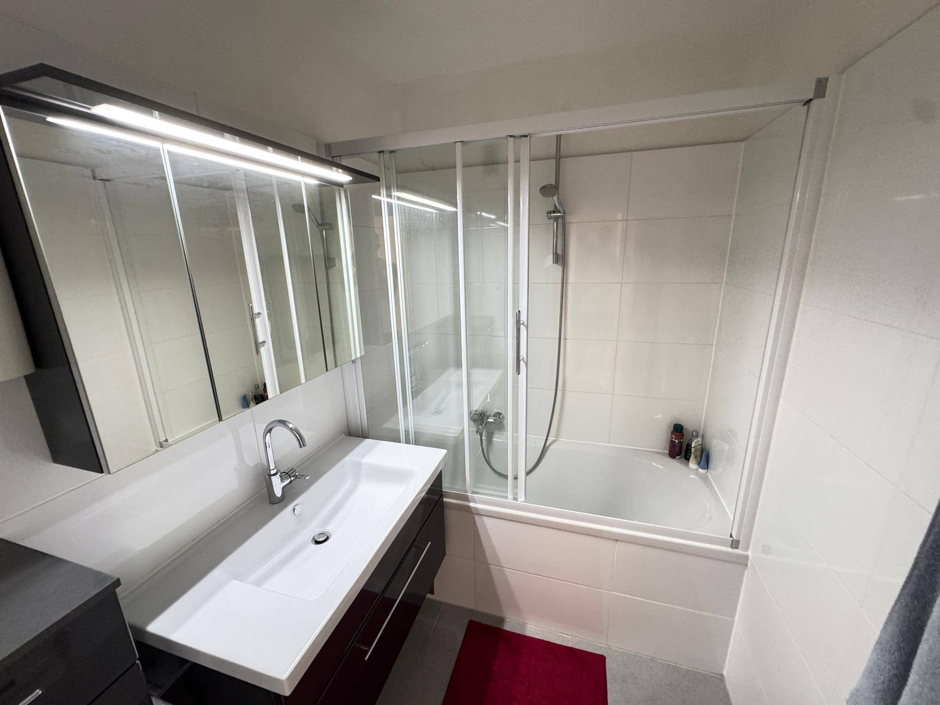 Modernes Badezimmer mit Badewanne, Duschabtrennung, Waschtisch und Spiegelschrank.