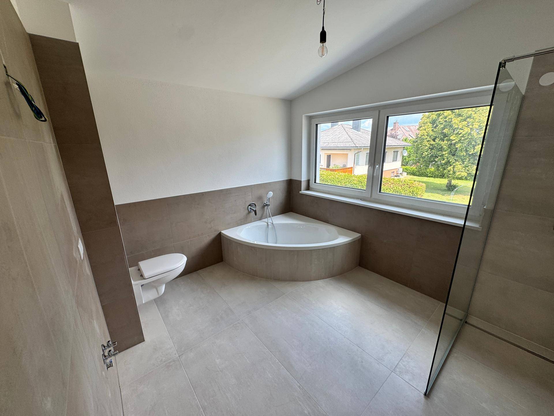 Helles Badezimmer mit moderner Ausstattung, Eckbadewanne, Dusche und Wand-WC.
