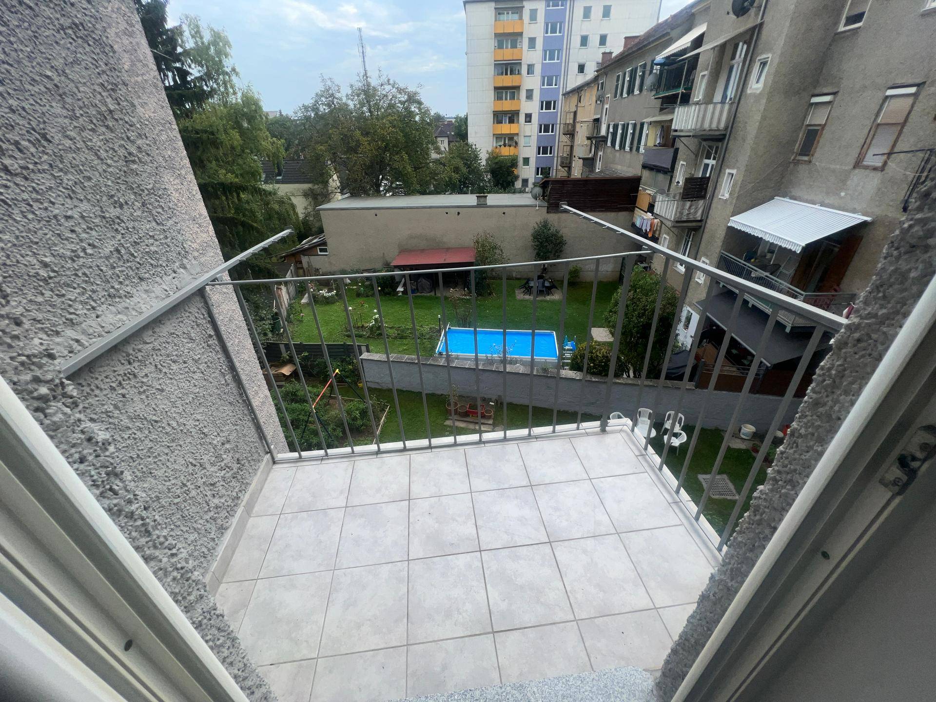 Balkon mit Fliesenboden und Blick auf den grünen Gemeinschaftsgarten mit Pool.