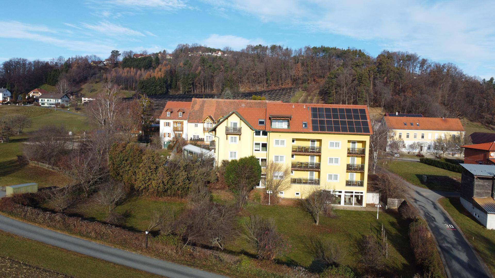 Luftaufnahme des Gebäudekomplexes mit Solaranlagen auf dem Dach und hügeliger Landschaft im Hintergrund.