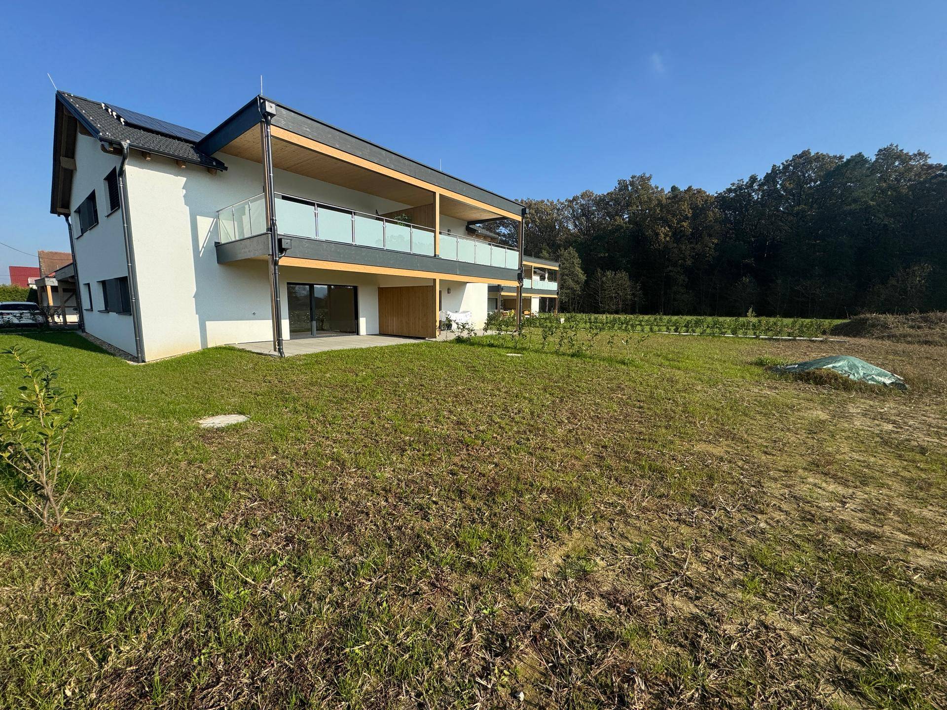 Moderne Doppelhaushälfte mit Balkon und Terrasse, umgeben von viel Grün.