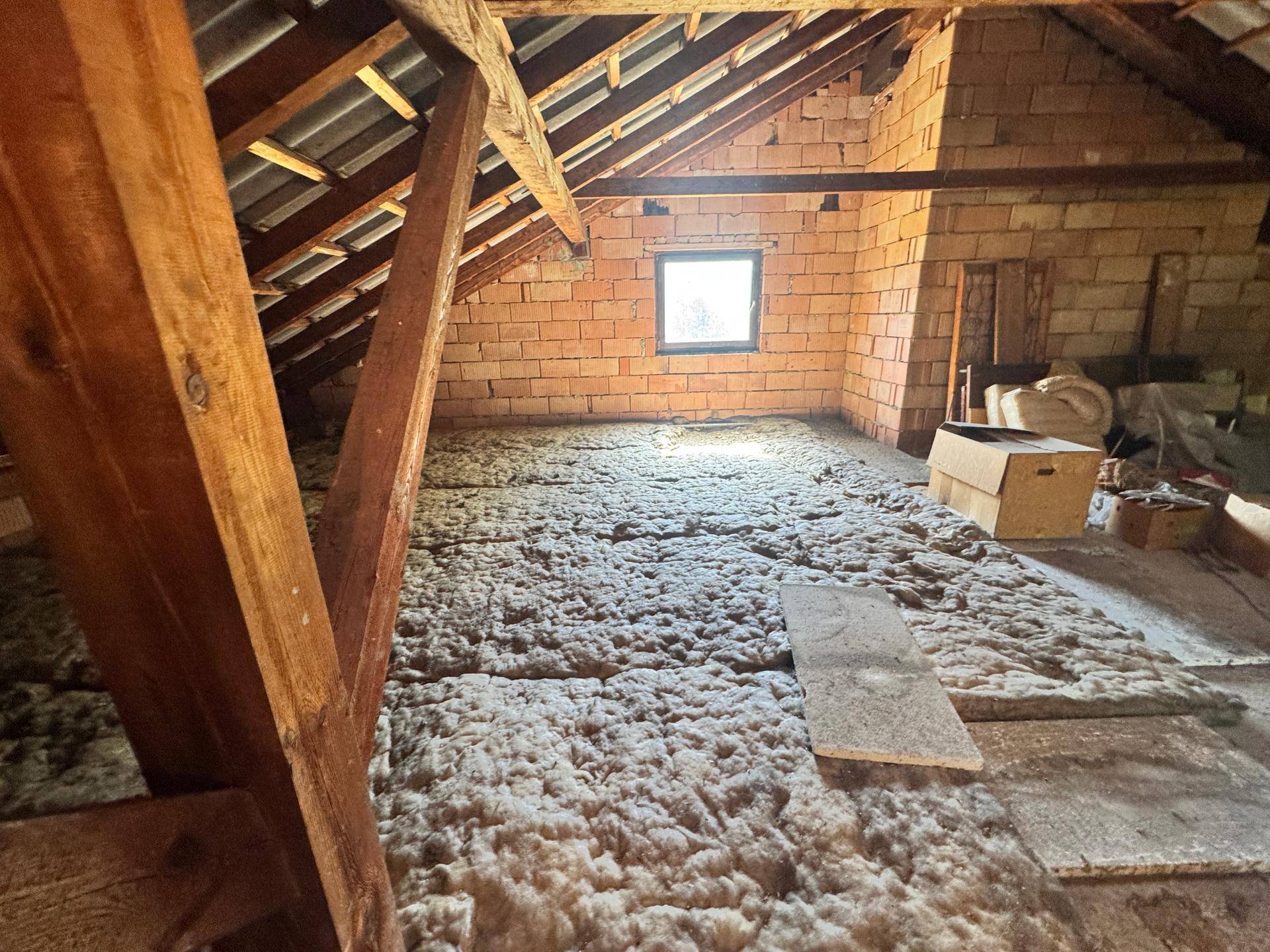 Helles Dachgeschoss mit sichtbaren Holzbalken und Isolierung, bereit für einen Ausbau.