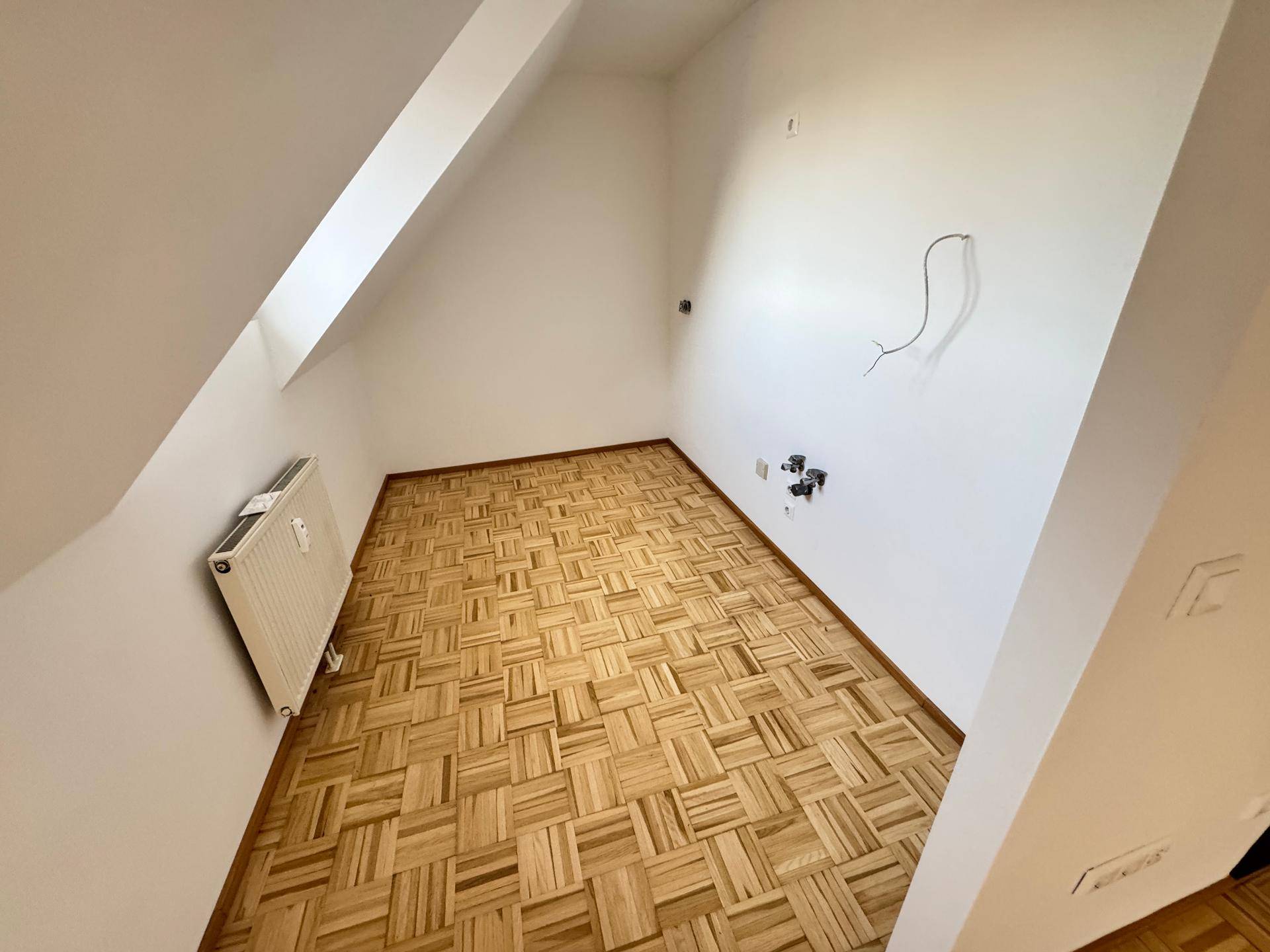 Kleineres Zimmer im Dachgeschoss mit Parkettboden, Dachschräge und Heizkörper.