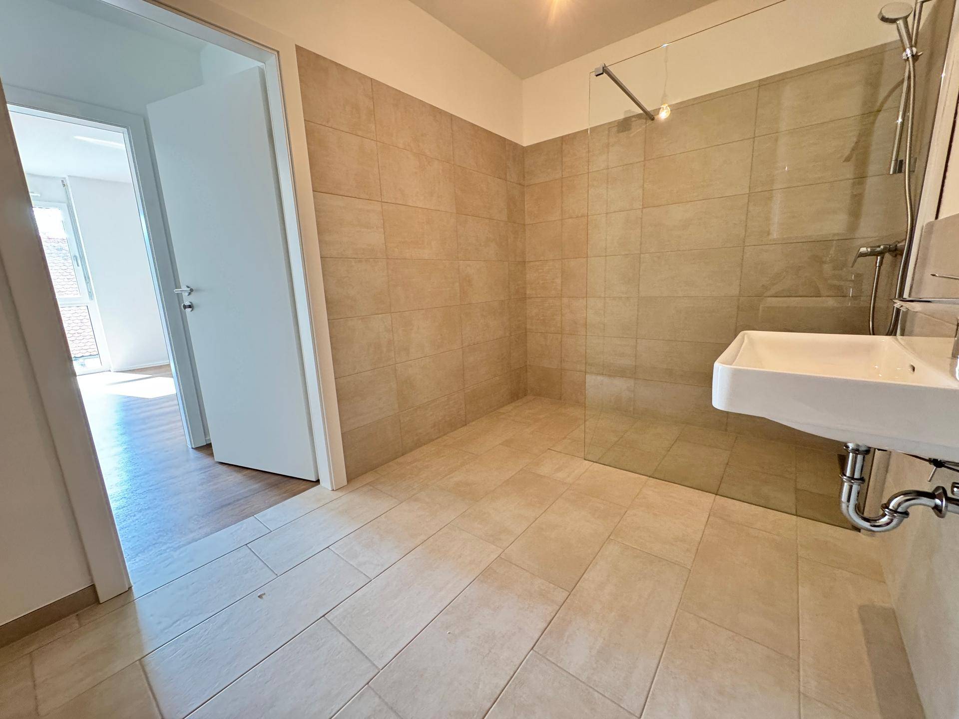 Helles Badezimmer mit begehbarer Dusche, modernem Waschbecken und Fliesenboden.