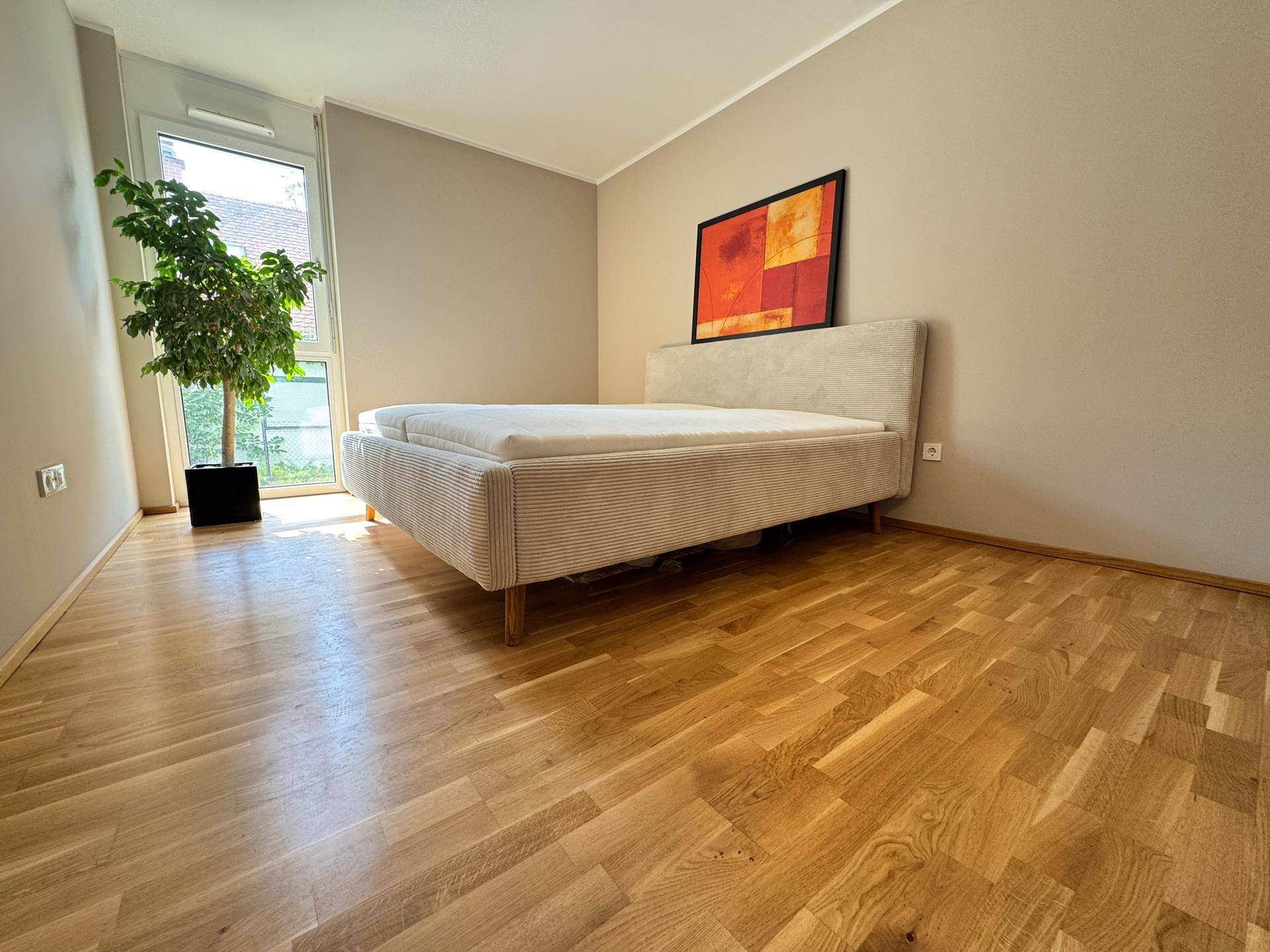 Schlafzimmer mit Holzboden, großem Fenster und einem Doppelbett, hell und freundlich gestaltet.