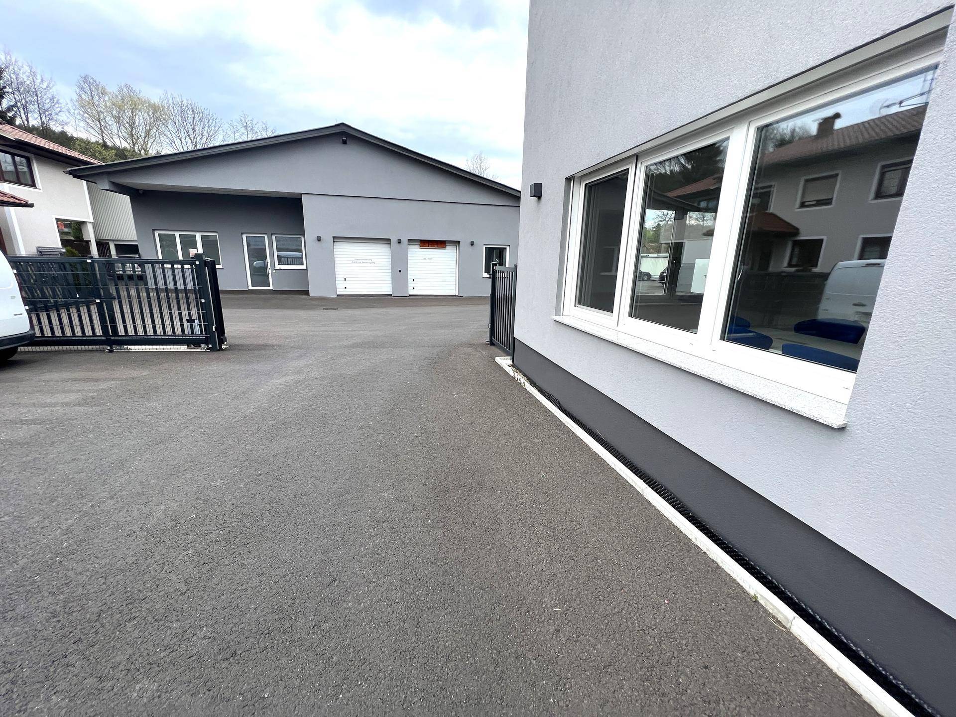 Außenansicht des modernen Geschäftsgebäudes mit angrenzendem Parkplatz und Nebengebäude unter bewölktem Himmel.