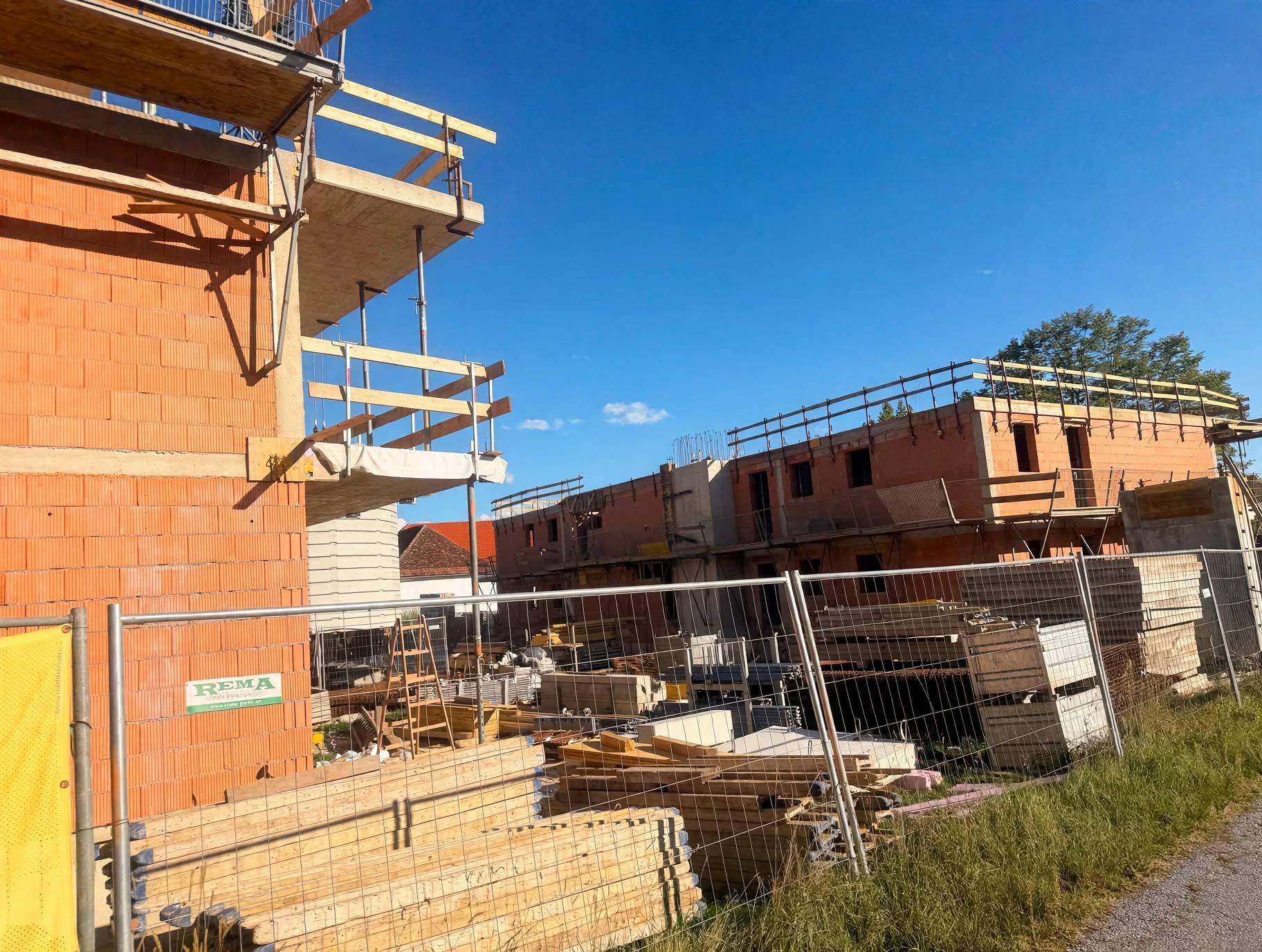 Baustelle mit gestapeltem Baumaterial und mehreren Rohbauten im Hintergrund unter blauem Himmel.