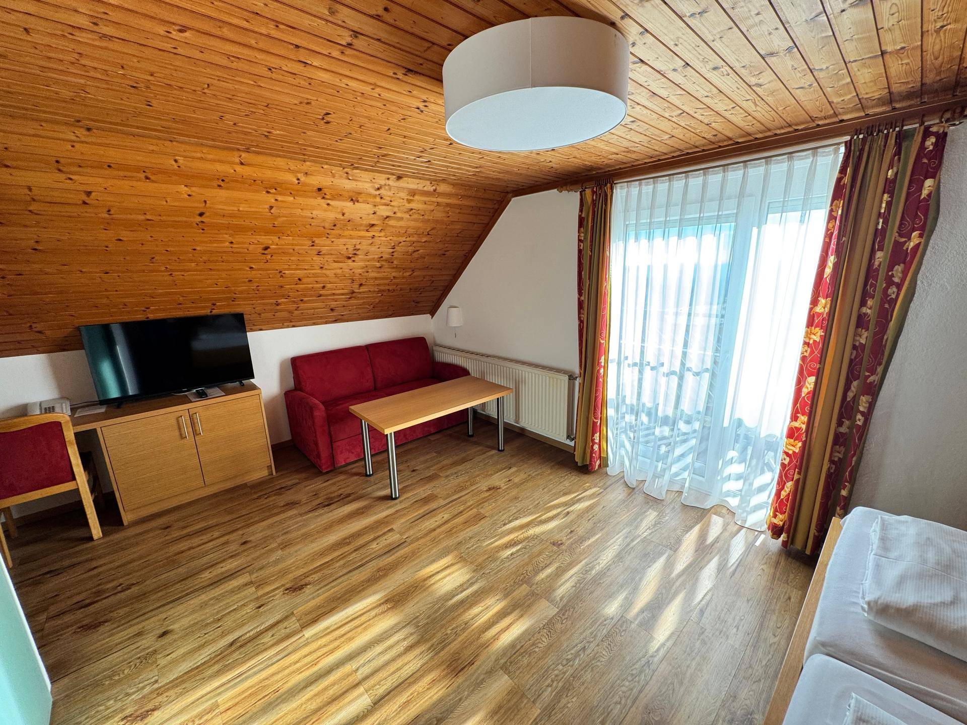 Schlafzimmer mit Holzbalkendecke, Sofa und Fernseher.