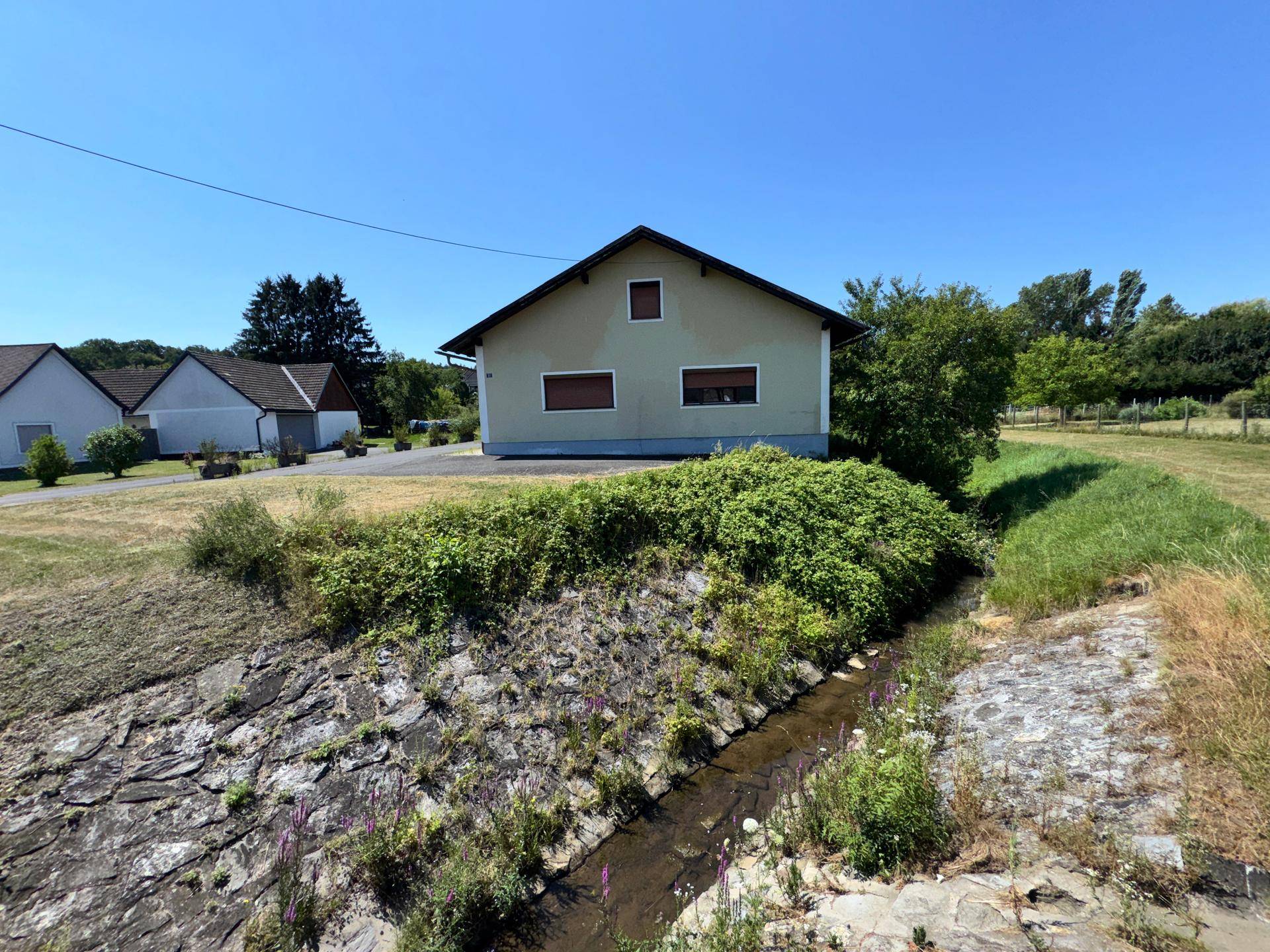 Rückansicht des Hauses mit angrenzendem Bachlauf und grüner Umgebung.