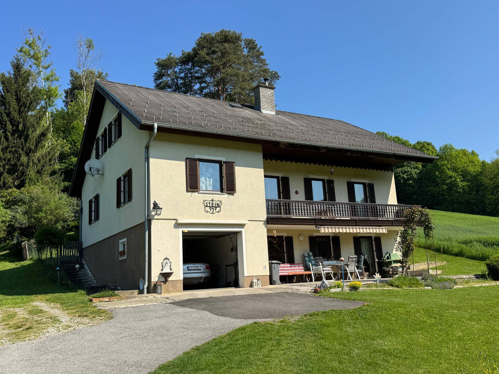 Vorderansicht eines Hauses mit Balkon, integrierter Garage und einer Terrasse mit Sitzgelegenheiten.