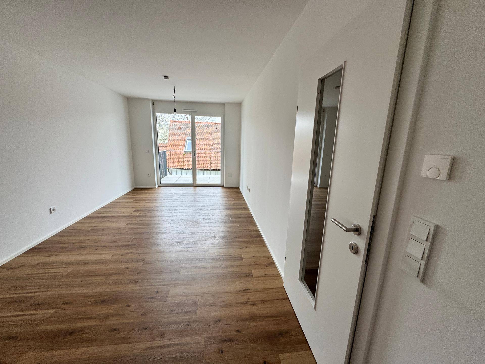 Heller Wohnbereich mit Holzboden und großer Schiebetür, die Zugang zu einem Balkon bietet.