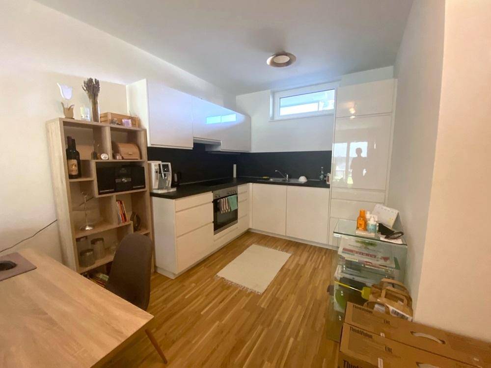 Moderne Einbauküche mit weißen Schränken, Holzboden und Fenster.