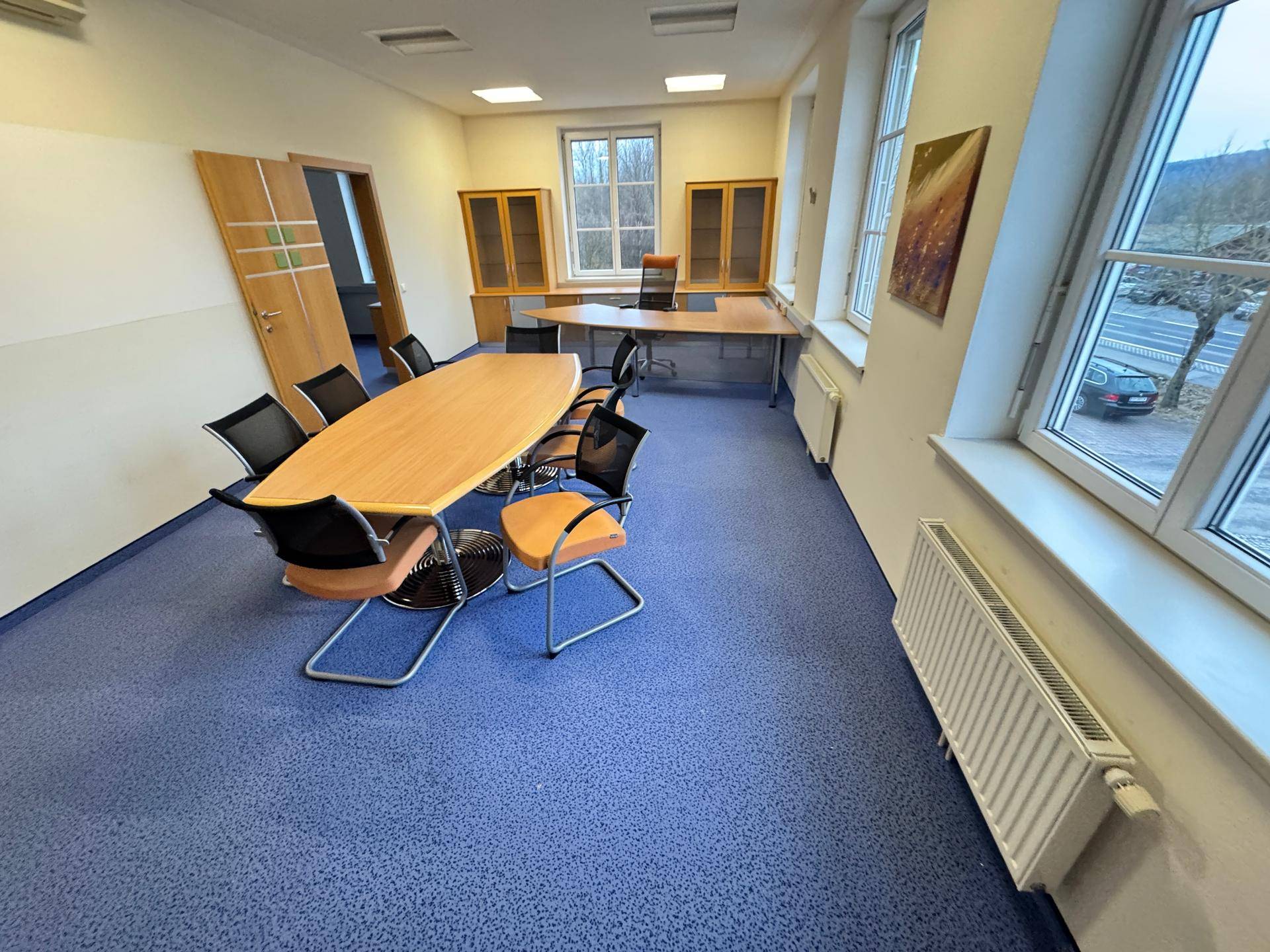 Großer Büroraum mit blauem Teppichboden, Konferenztisch und mehreren Fenstern.