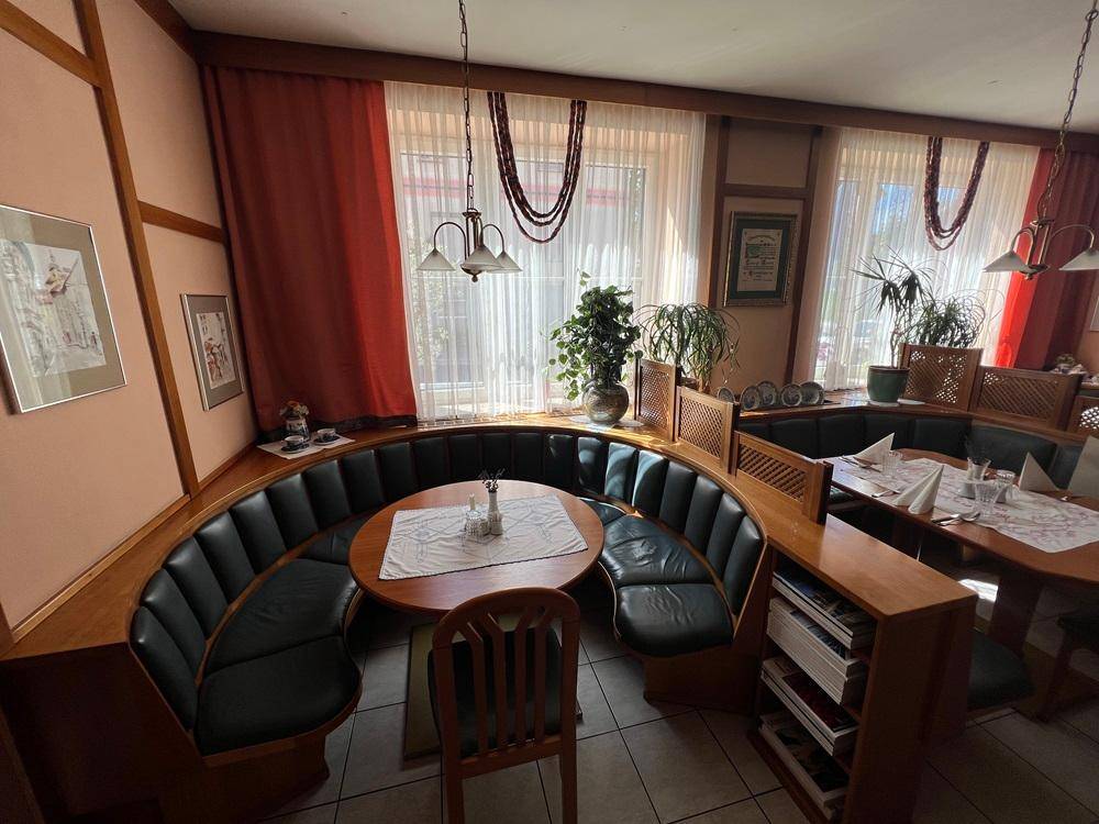 Restaurantbereich mit runden Tischen, gepolsterten Sitzbänken und großen Fenstern.