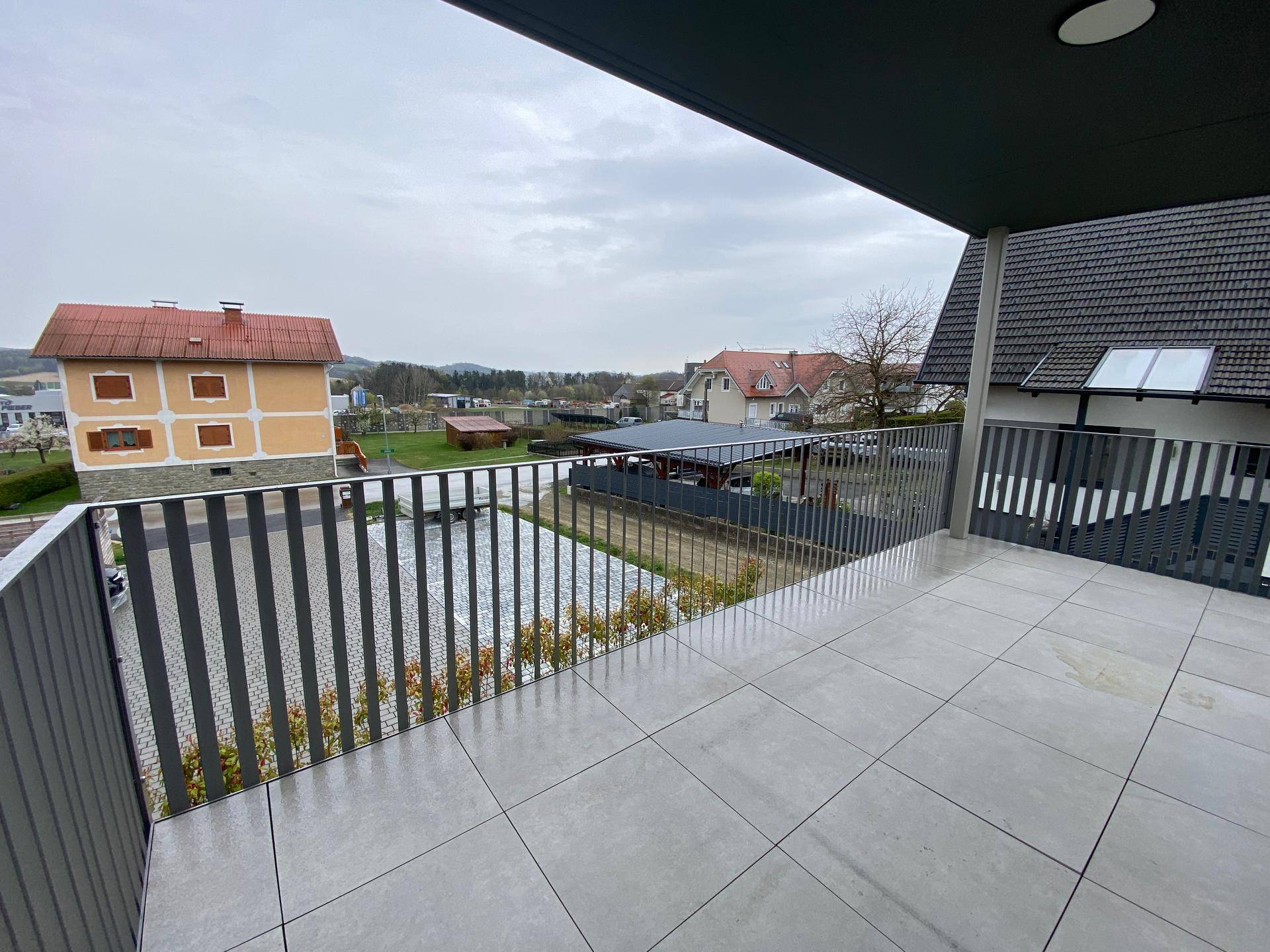 Balkon mit Fliesenboden und Blick über die umliegende Wohngegend und grüne Hügel.