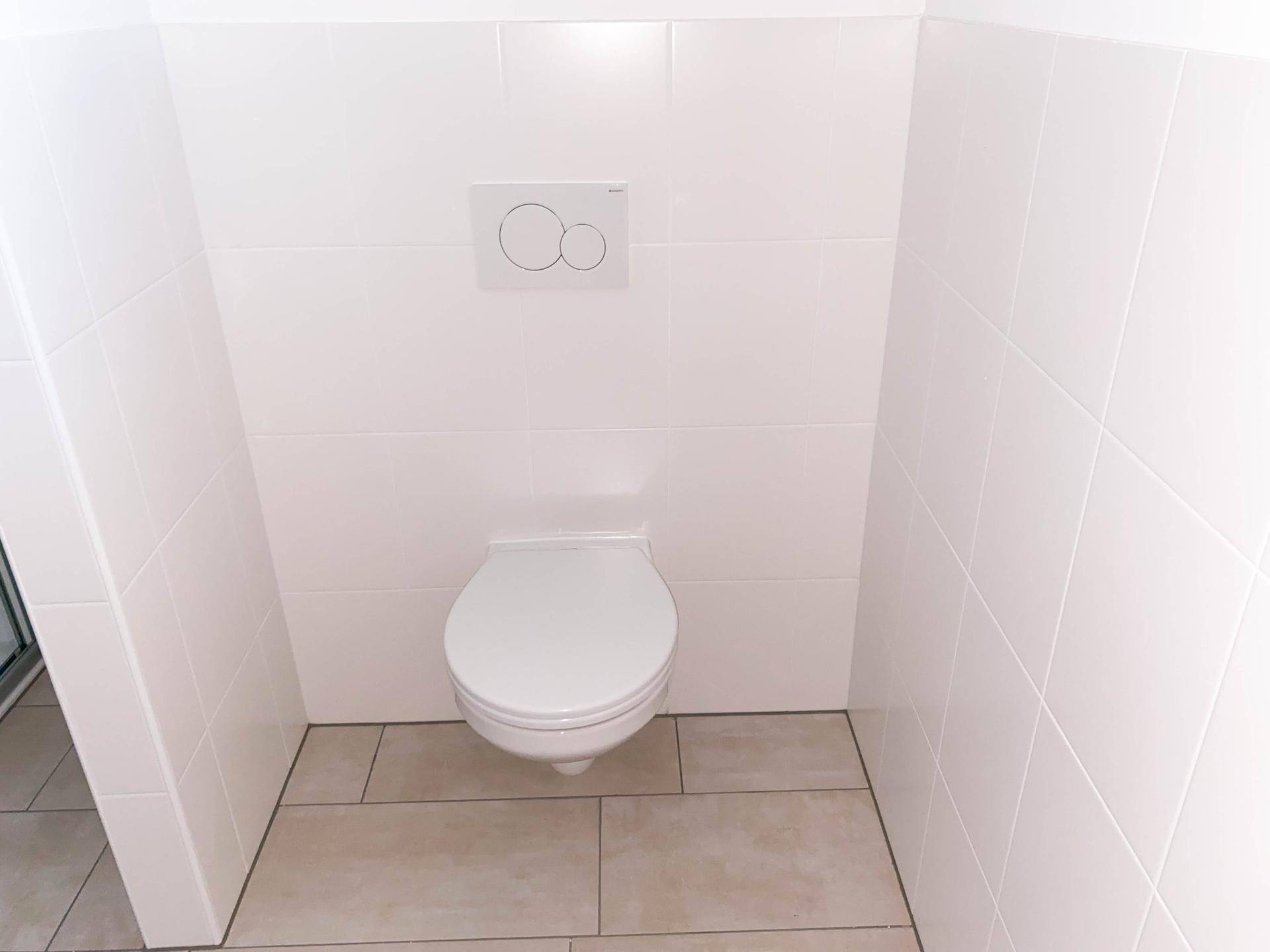 Wandhängendes WC mit moderner Spülung und weißen Fliesen, sauber und funktional.