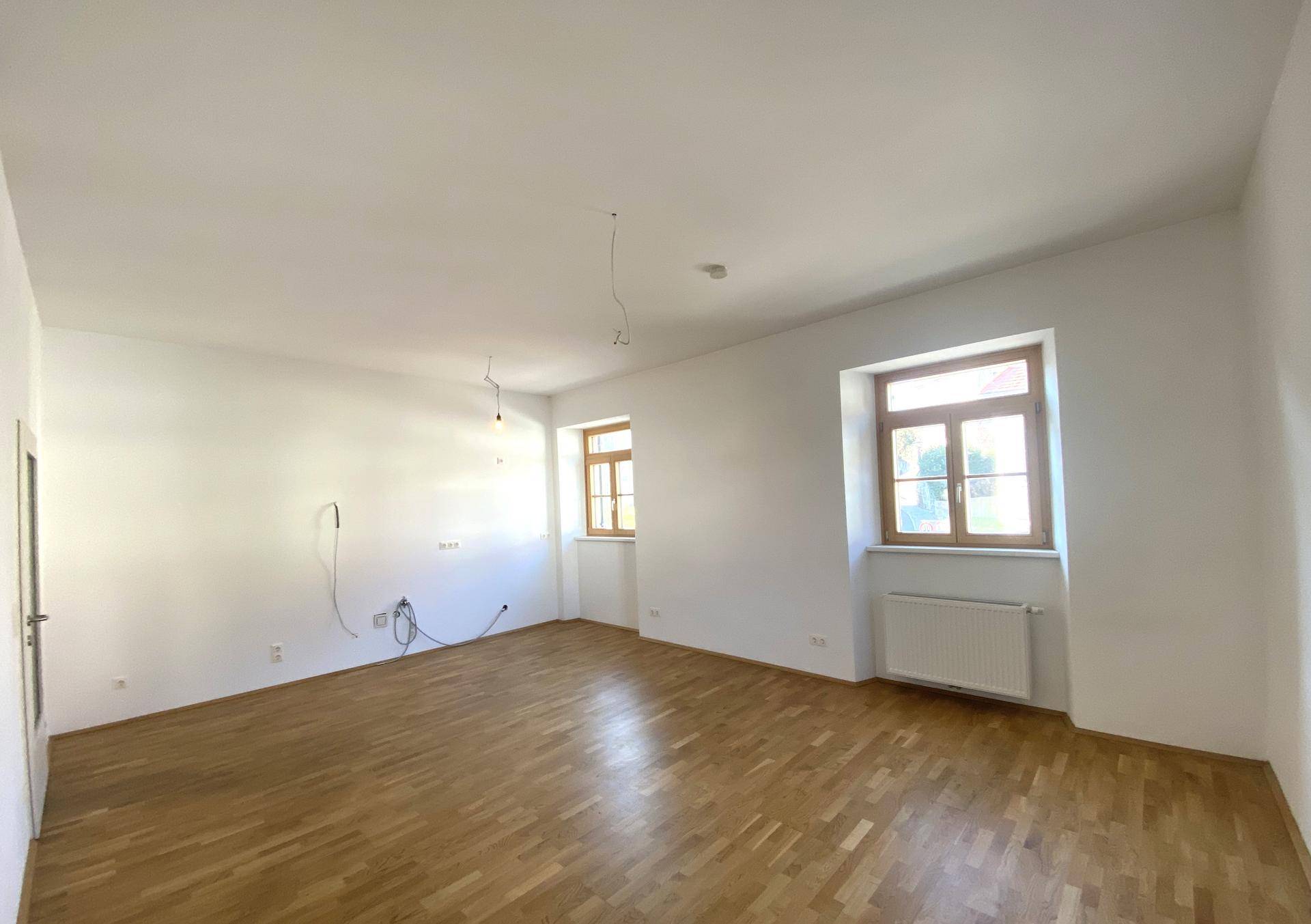 Geräumiges Zimmer mit Parkettboden, weißen Wänden und mehreren Fenstern, ideal für einen Wohnbereich.