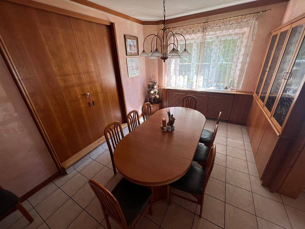 Esszimmer mit großem Holztisch, passenden Stühlen und einem Fliesenboden unter einer Holzdecke.
