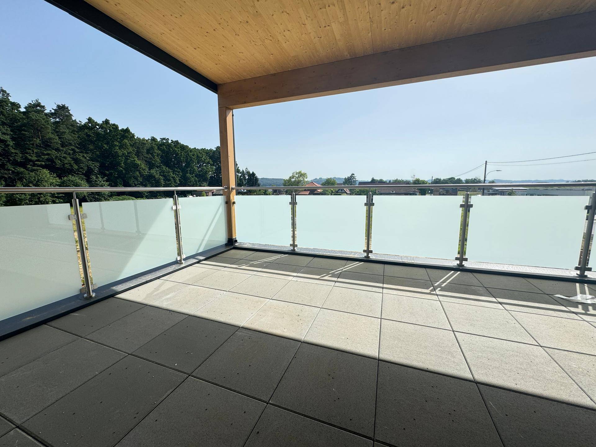 Überdachter Balkon mit Fliesenboden, Glasgeländer und weitem Blick in die Landschaft.