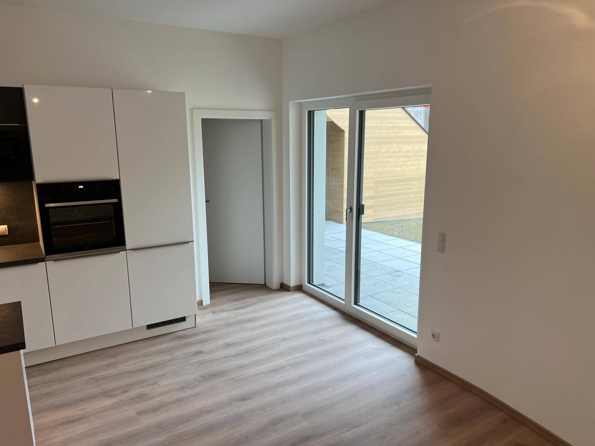 Offener Wohnbereich mit moderner Küche und großer Schiebetür, die zur Terrasse führt.