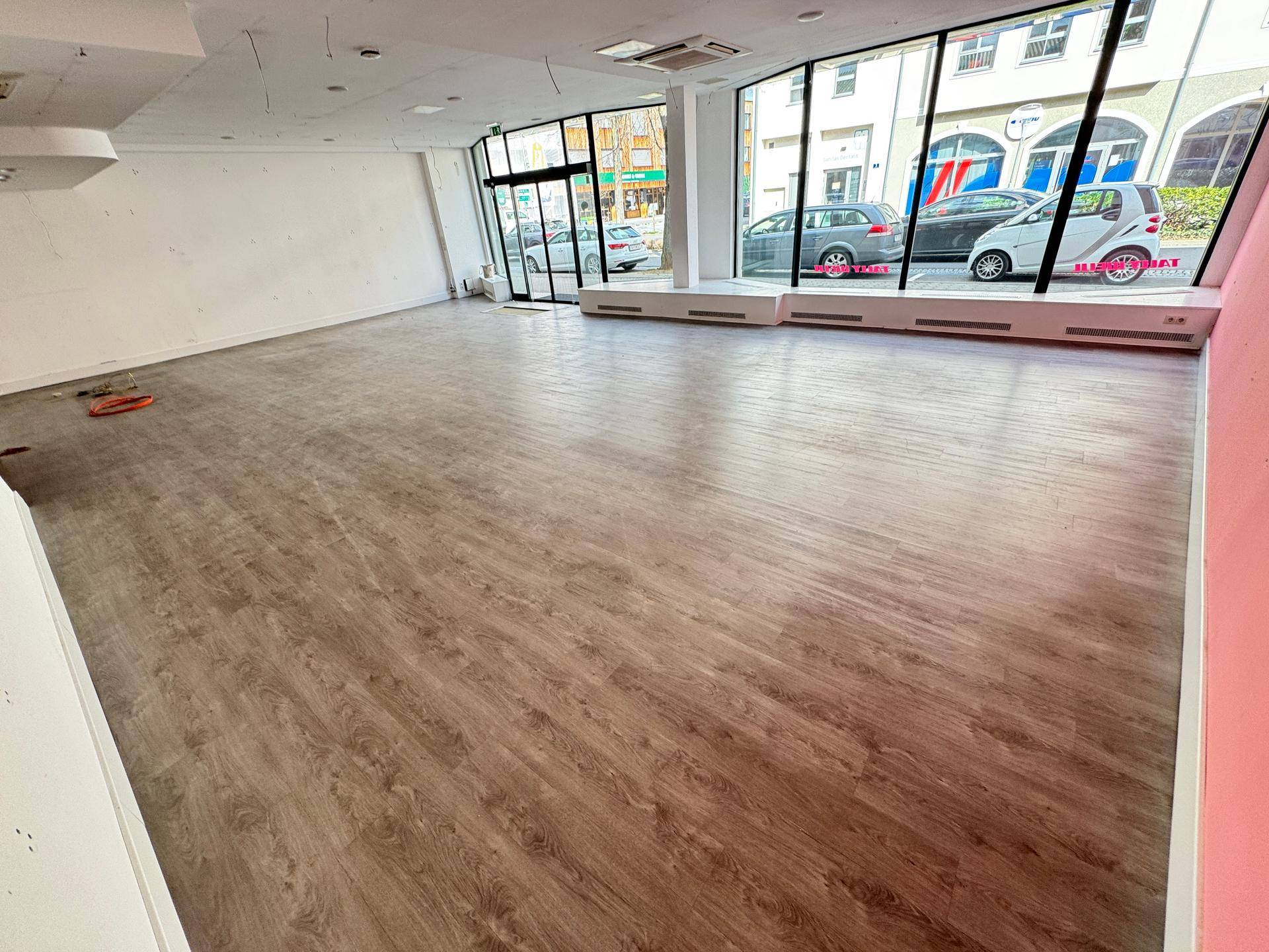 Weitläufiger Ladenbereich mit Laminatboden und viel Tageslicht durch die Schaufenster.