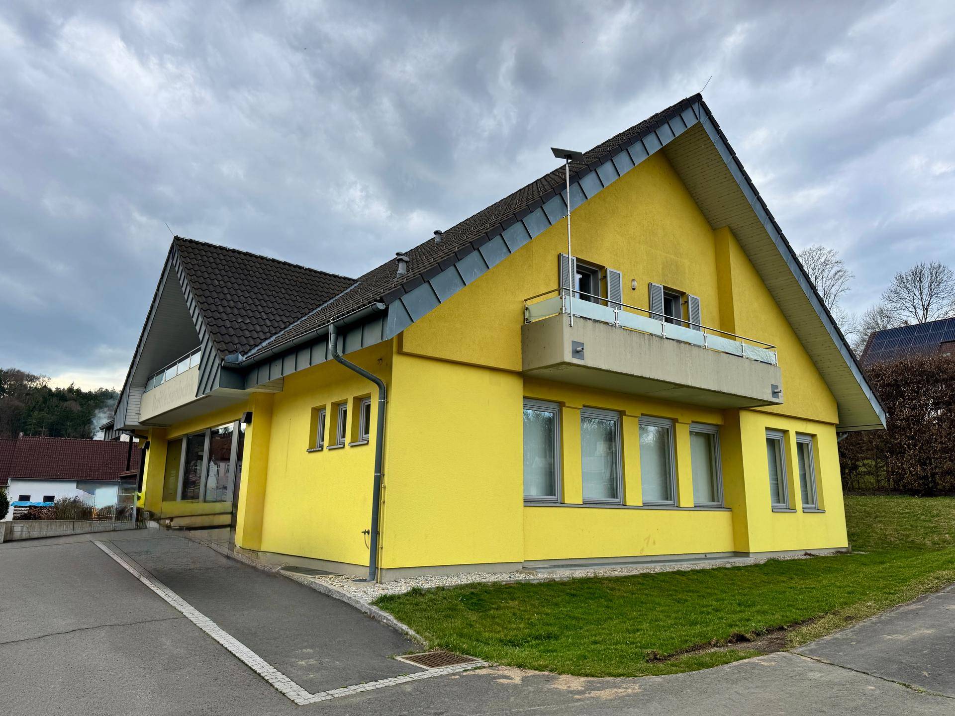 Seitenansicht des gelben Gebäudes mit Balkon und Fenstern unter bewölktem Himmel.