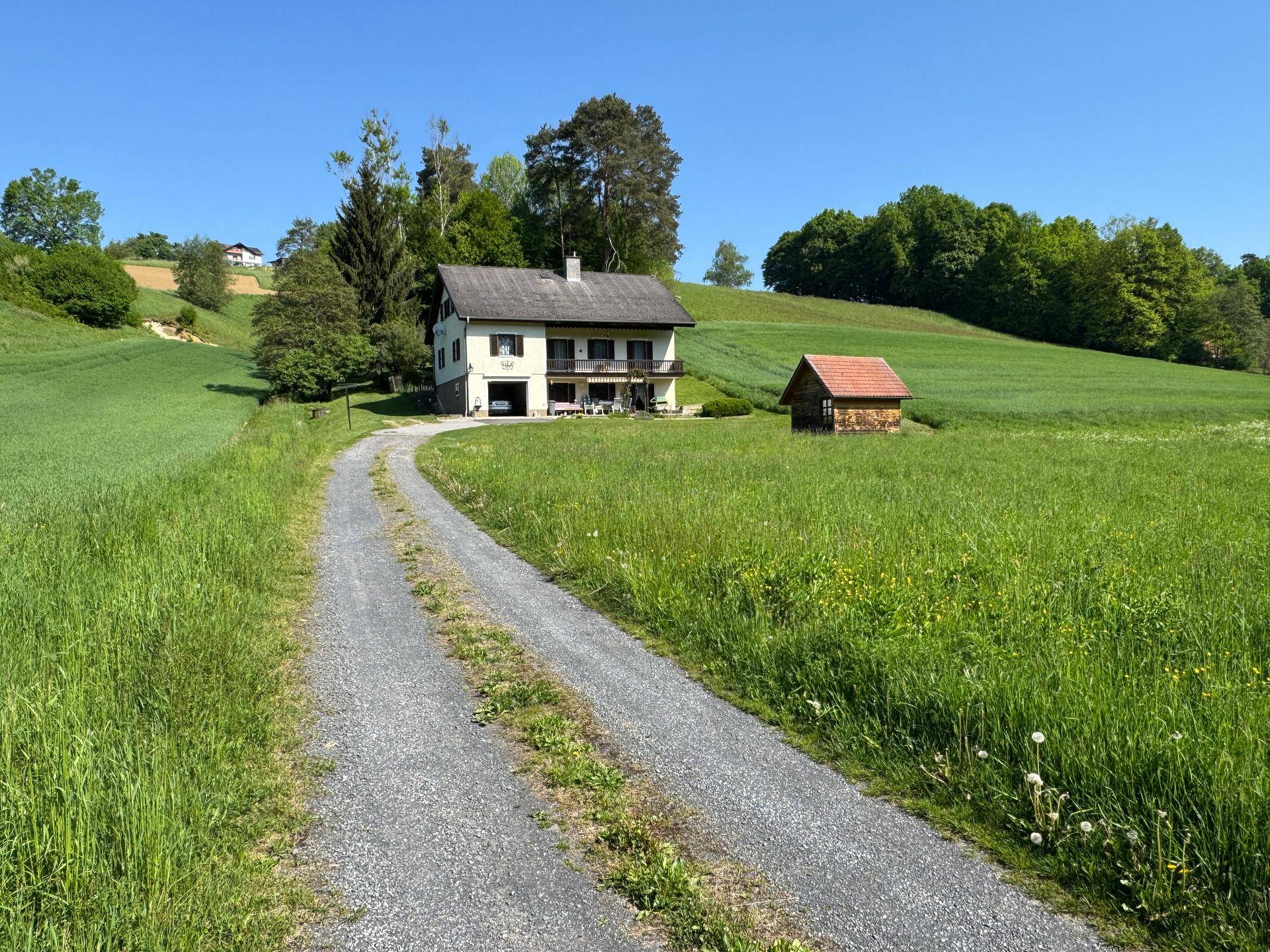 Landhaus mit Zufahrt und Gartenhaus, eingebettet in eine idyllische grüne Landschaft.