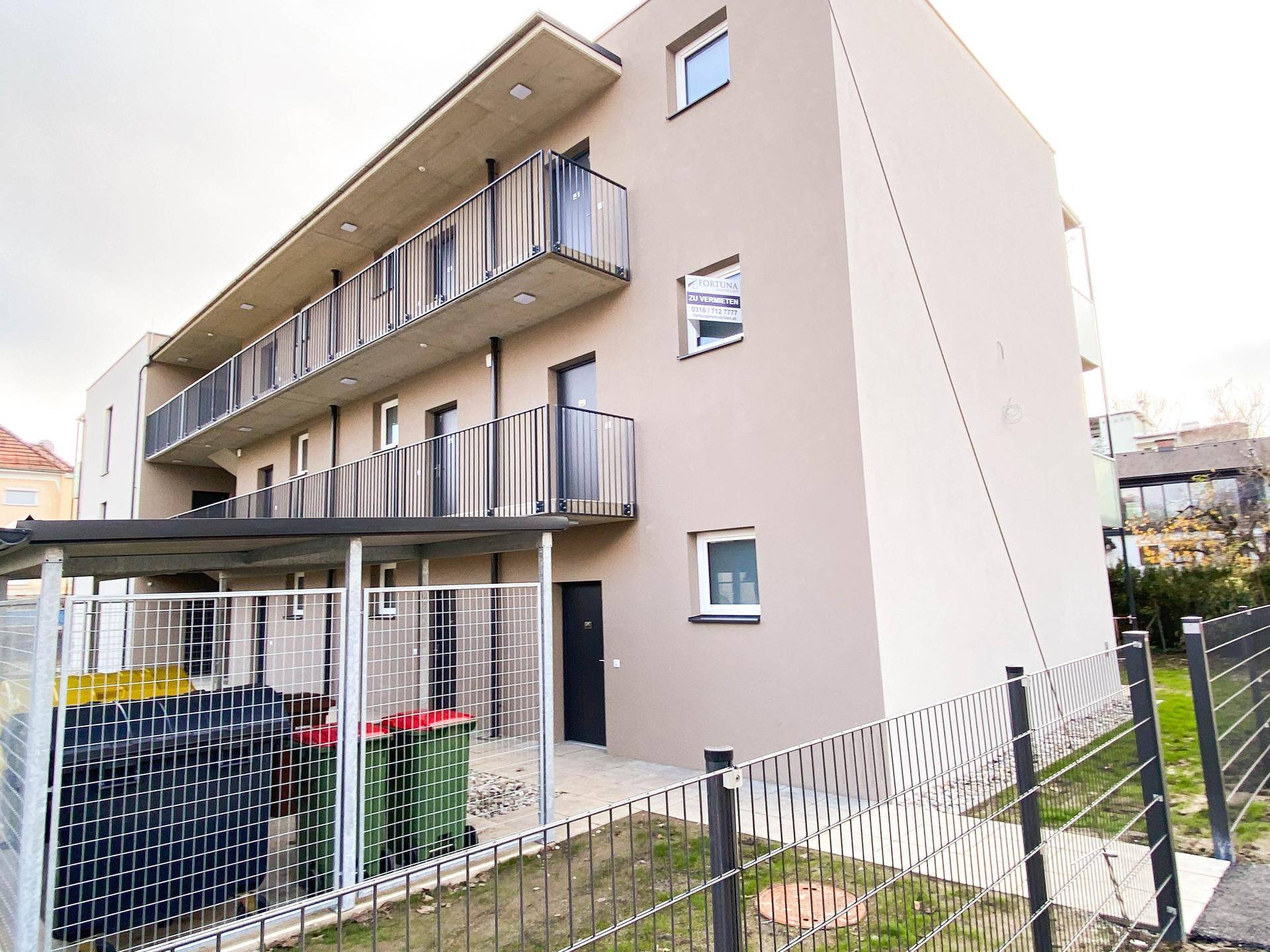 Seitenansicht des Gebäudes mit Balkonen, Carport und Mülltonnenbereich.